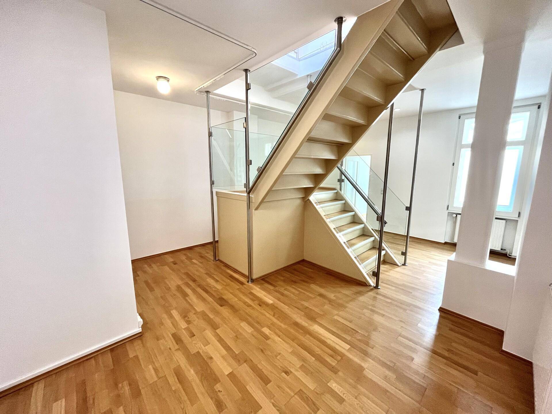 Offener Wohnbereich mit einer eleganten Holztreppe und Glasgeländer, die den Raum strukturiert.