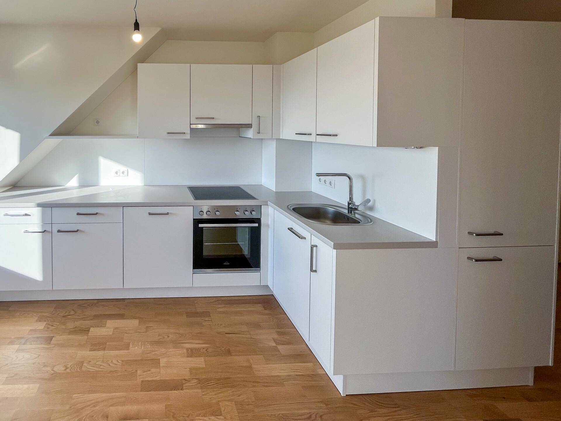 Moderne Einbauküche mit weißen Schränken, Kochfeld und Backofen unter Dachschräge.