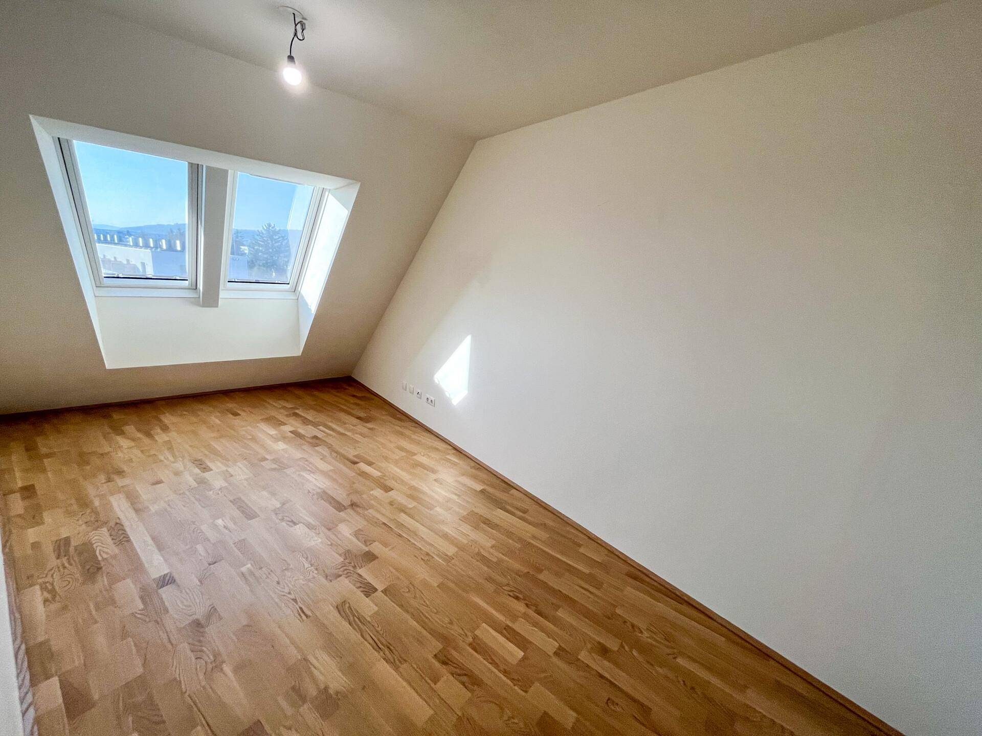 Helles Schlafzimmer mit Dachfenstern, Parkettboden und schrägen Wänden.