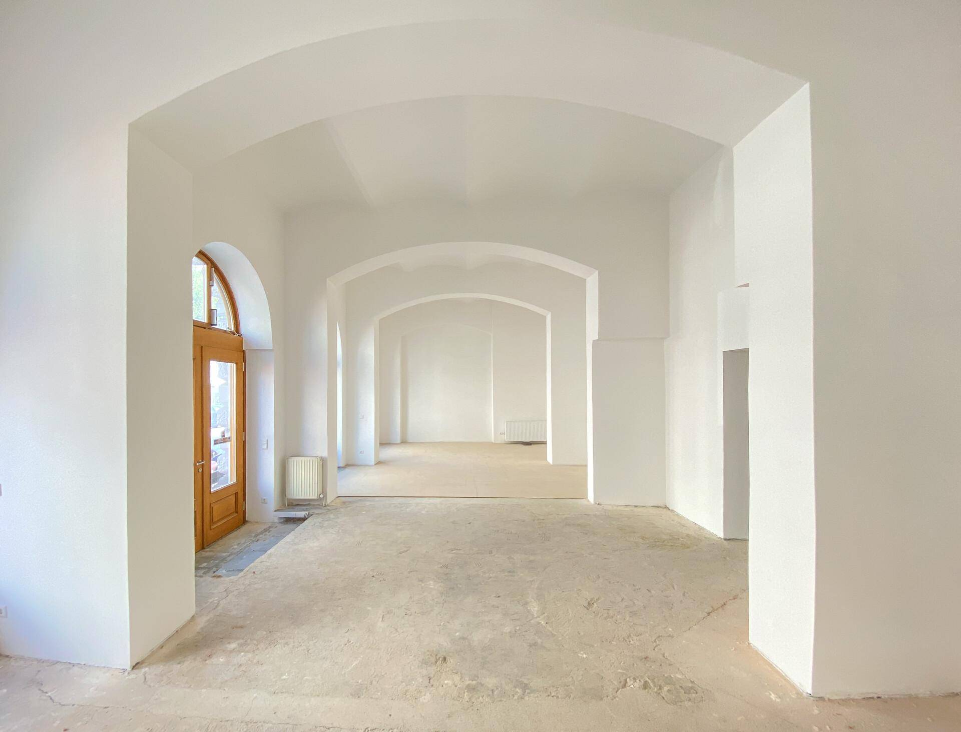 Heller, offener Innenraum mit hohen Gewölbedecken, Holztür und Rundbogenfenstern, die den Raum mit Licht füllen.