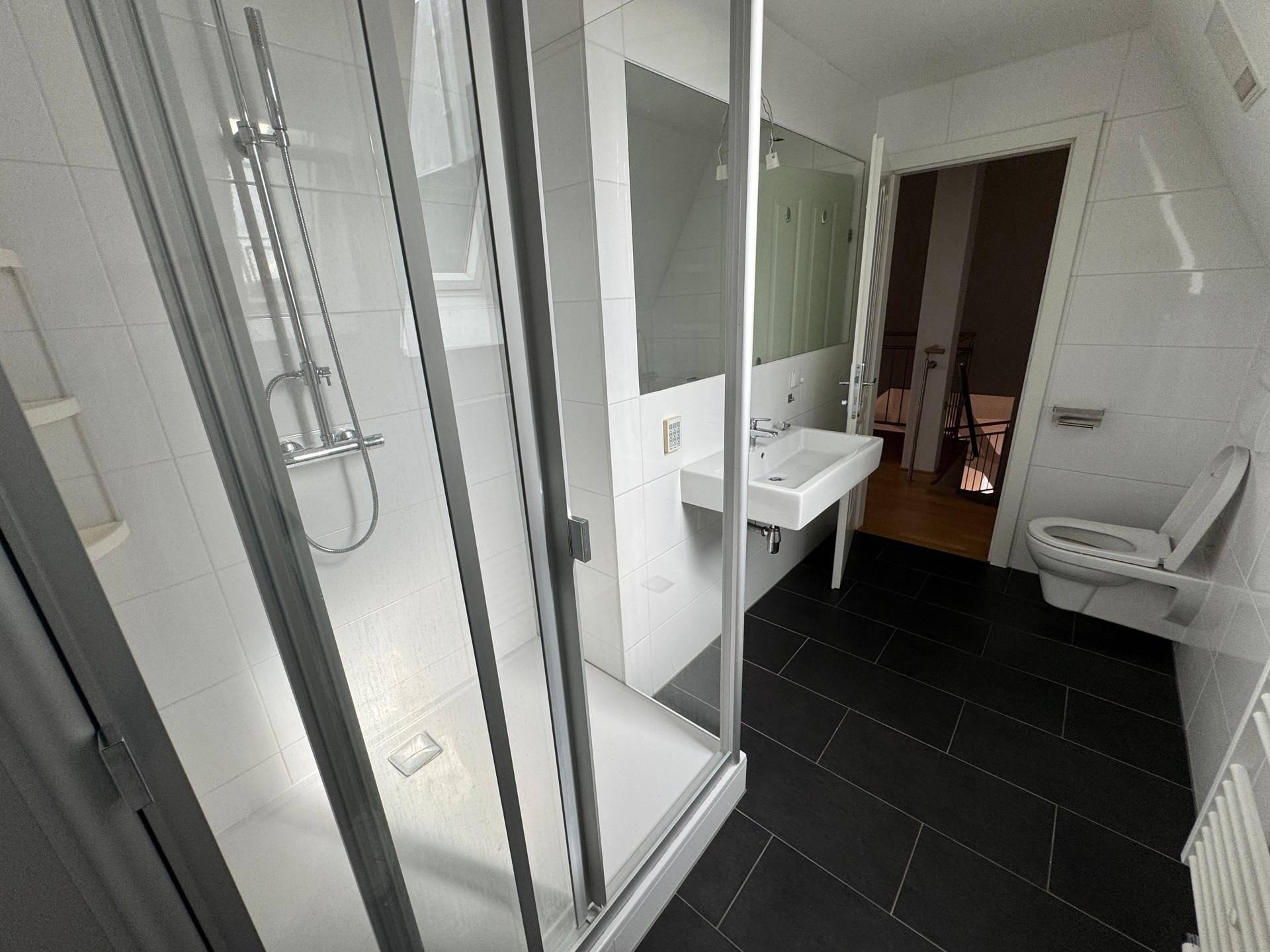 Helles Badezimmer mit Duschkabine, wandhängendem WC und dunklen Bodenfliesen.