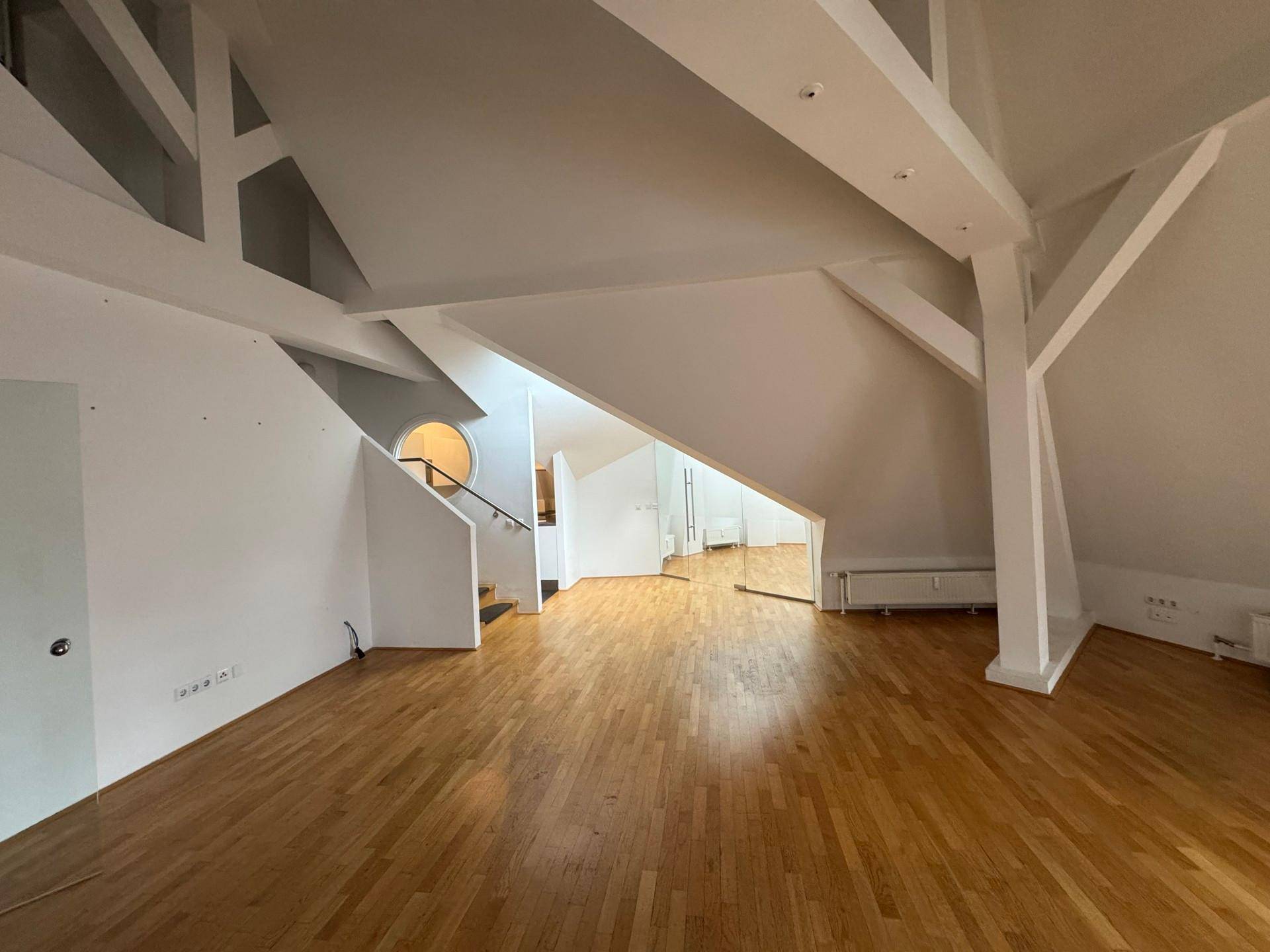 Geräumiger Wohnbereich mit Holzboden, sichtbaren Dachbalken und charakteristischen schrägen Wänden.