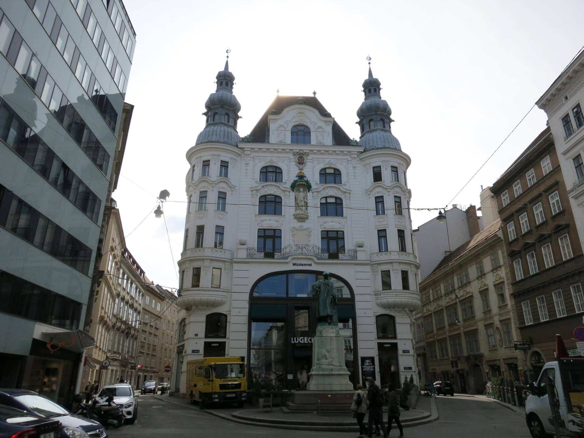 Historisches Gebäude an einer belebten Straßenecke in Wien mit markanter Architektur und Statuen.