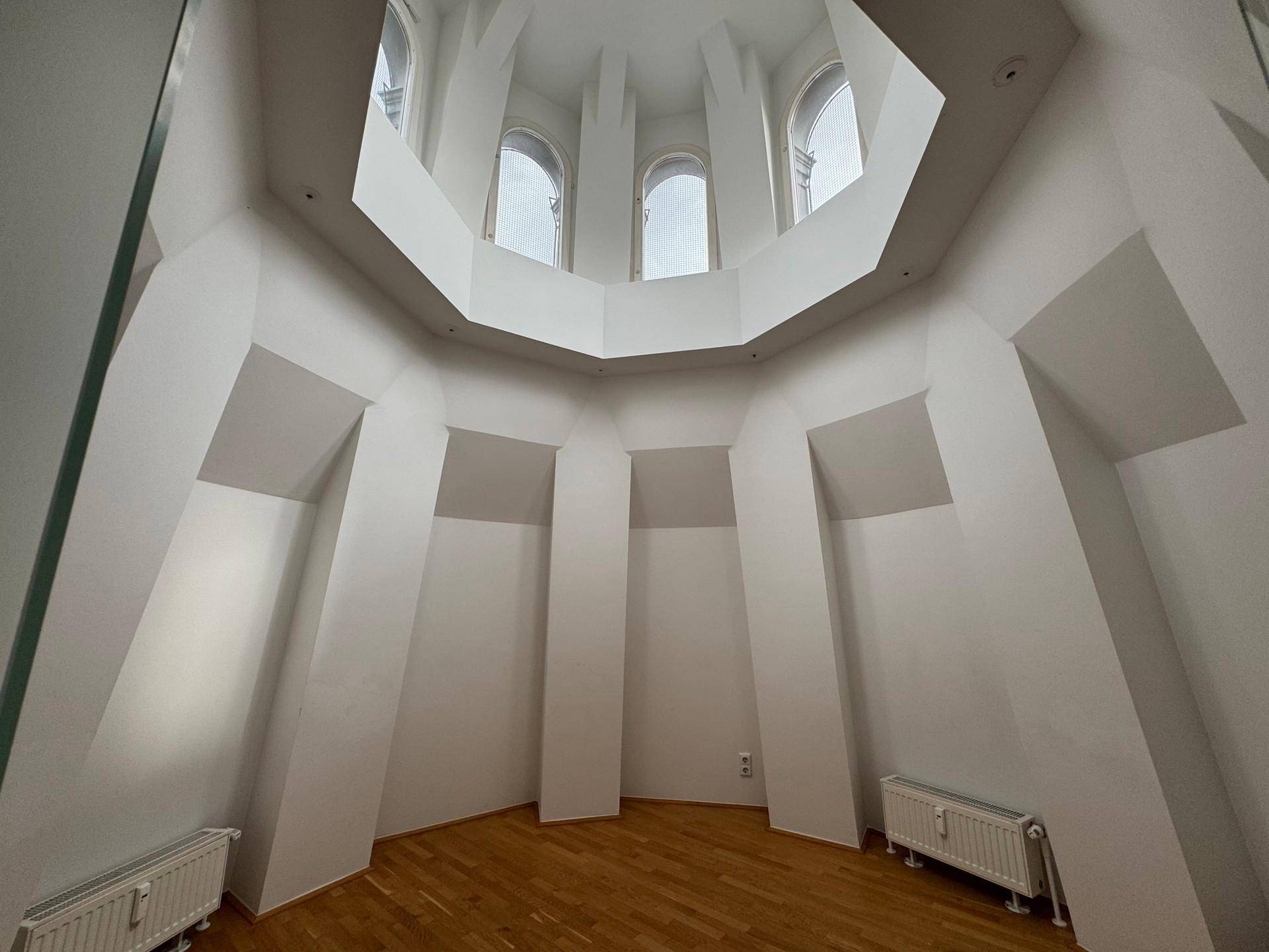 Hoher, heller Raum mit gewölbter Decke und hohen Bogenfenstern, die viel Tageslicht hereinlassen.