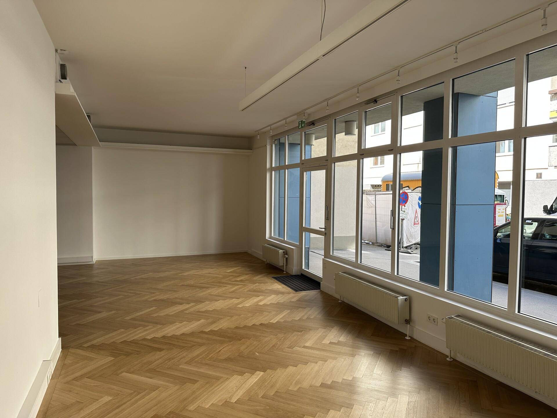 Heller und geräumiger Bürobereich mit Fischgrätparkett und einer langen Fensterfront zur Straße.