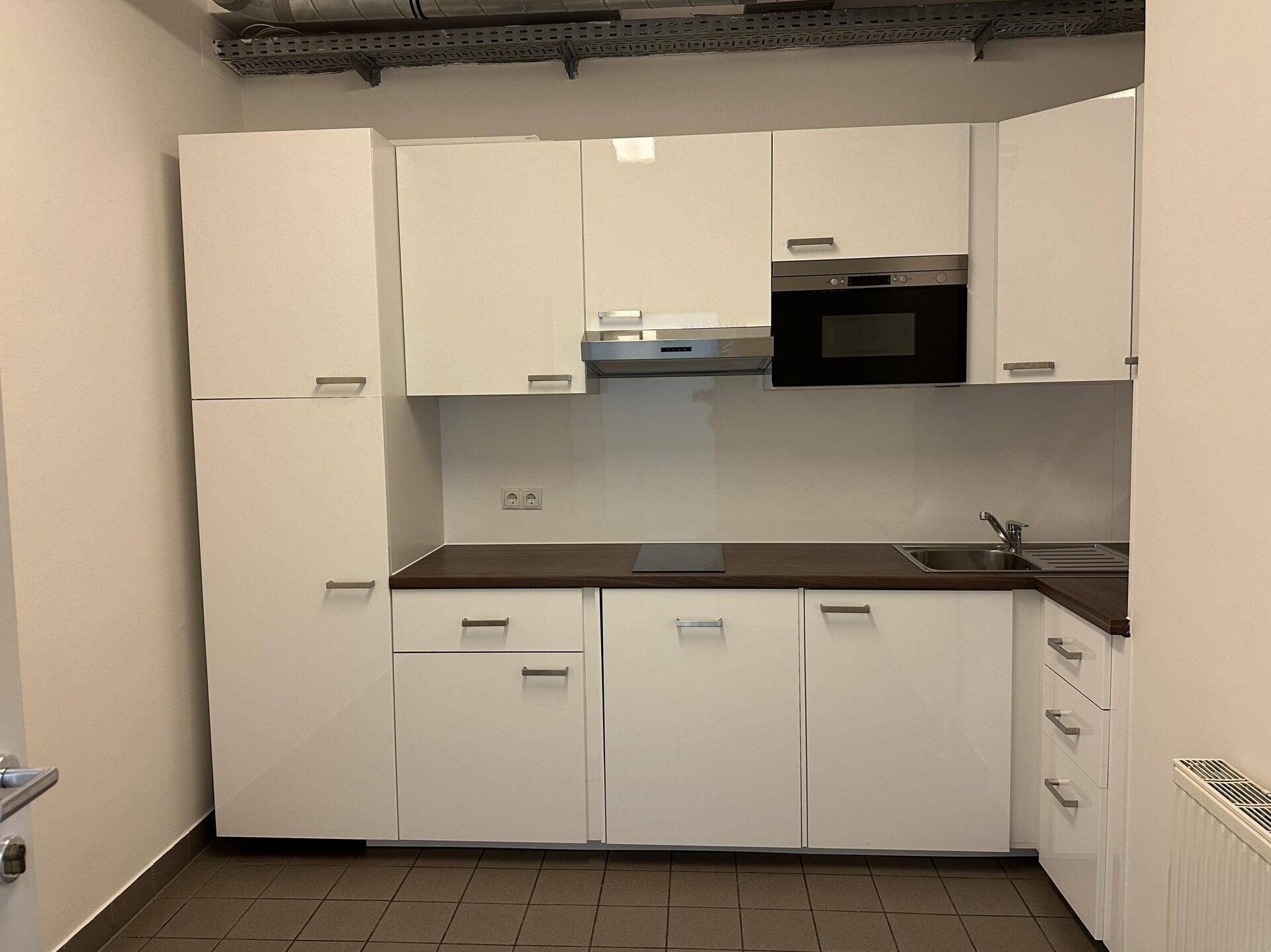 Moderne Küchenzeile mit weißen Hochglanzschränken, integrierten Geräten und dunkler Arbeitsplatte.
