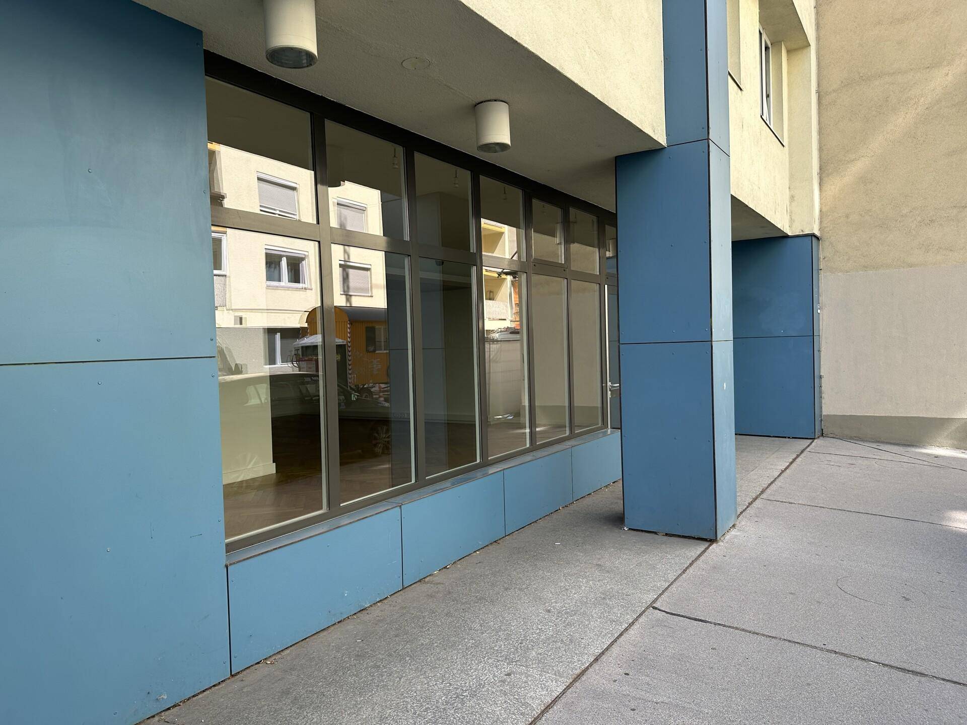 Außenansicht des Gebäudes mit blauen Paneelen und großen Schaufenstern im Erdgeschoss.
