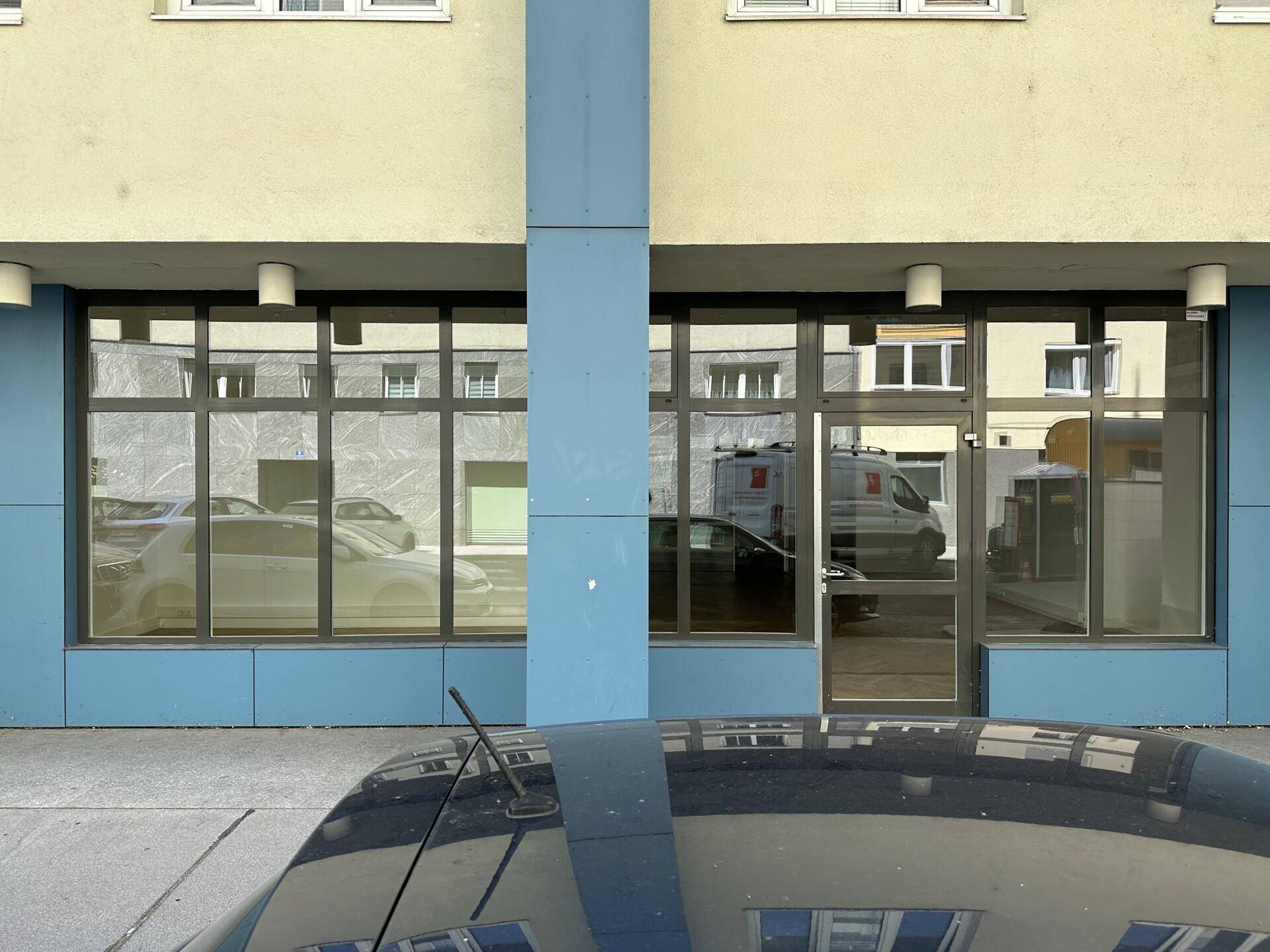 Fassade eines Geschäftsgebäudes mit großen Schaufenstern und blauen Verkleidungen im Erdgeschoss.