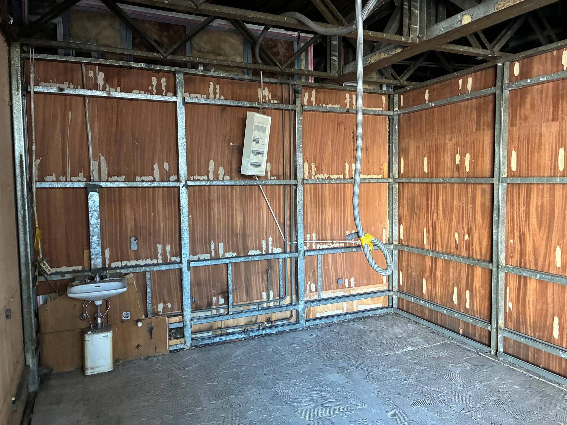 Innenraum im Rohbau mit Metallständerwerk, Holzverkleidung und sichtbaren Installationen für ein Waschbecken.