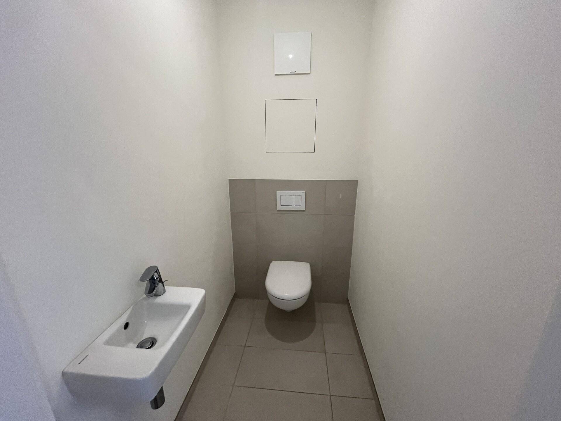 Modernes Gäste-WC mit Wand-WC, kleinem Waschbecken und hellen Fliesen an der Wand.