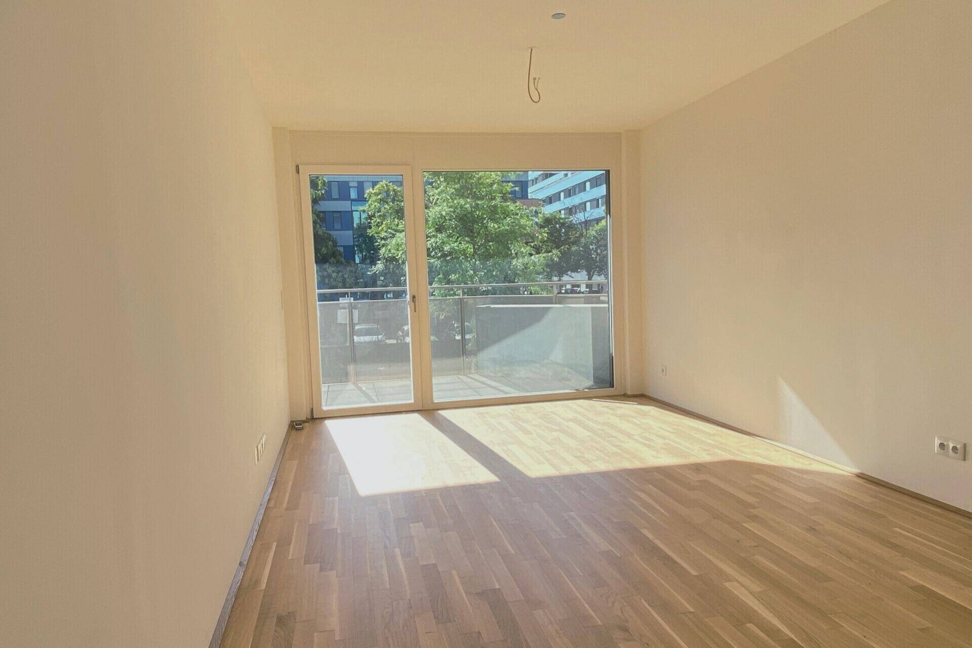 Heller Wohnraum mit Parkettboden und Zugang zu einem Balkon, durchflutet von Sonnenlicht.