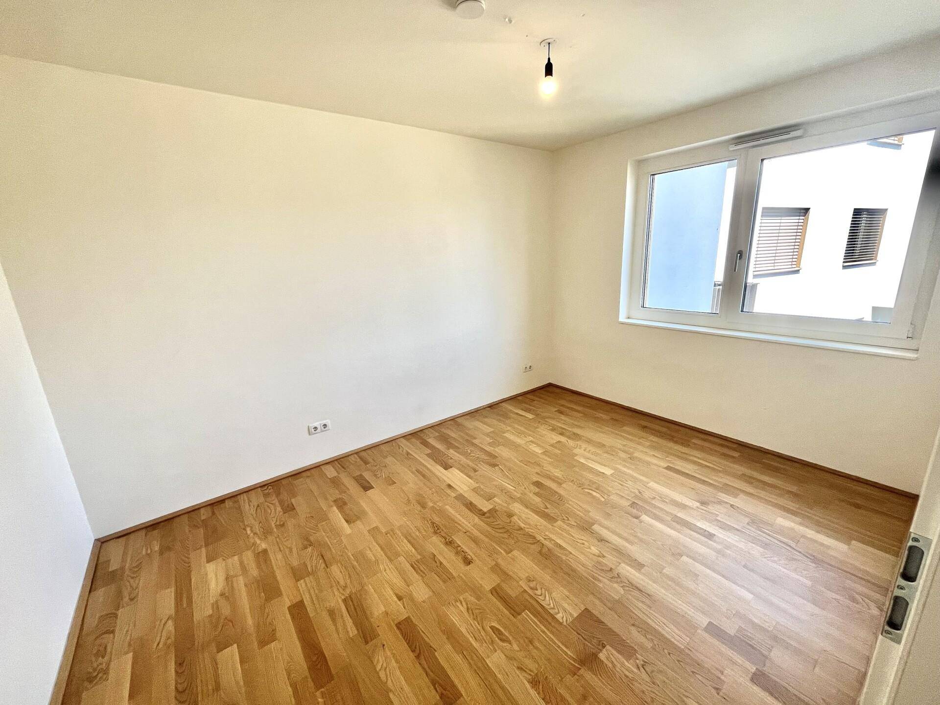 Helles Schlafzimmer mit Parkettboden und großem Fenster, bereit zur individuellen Einrichtung.