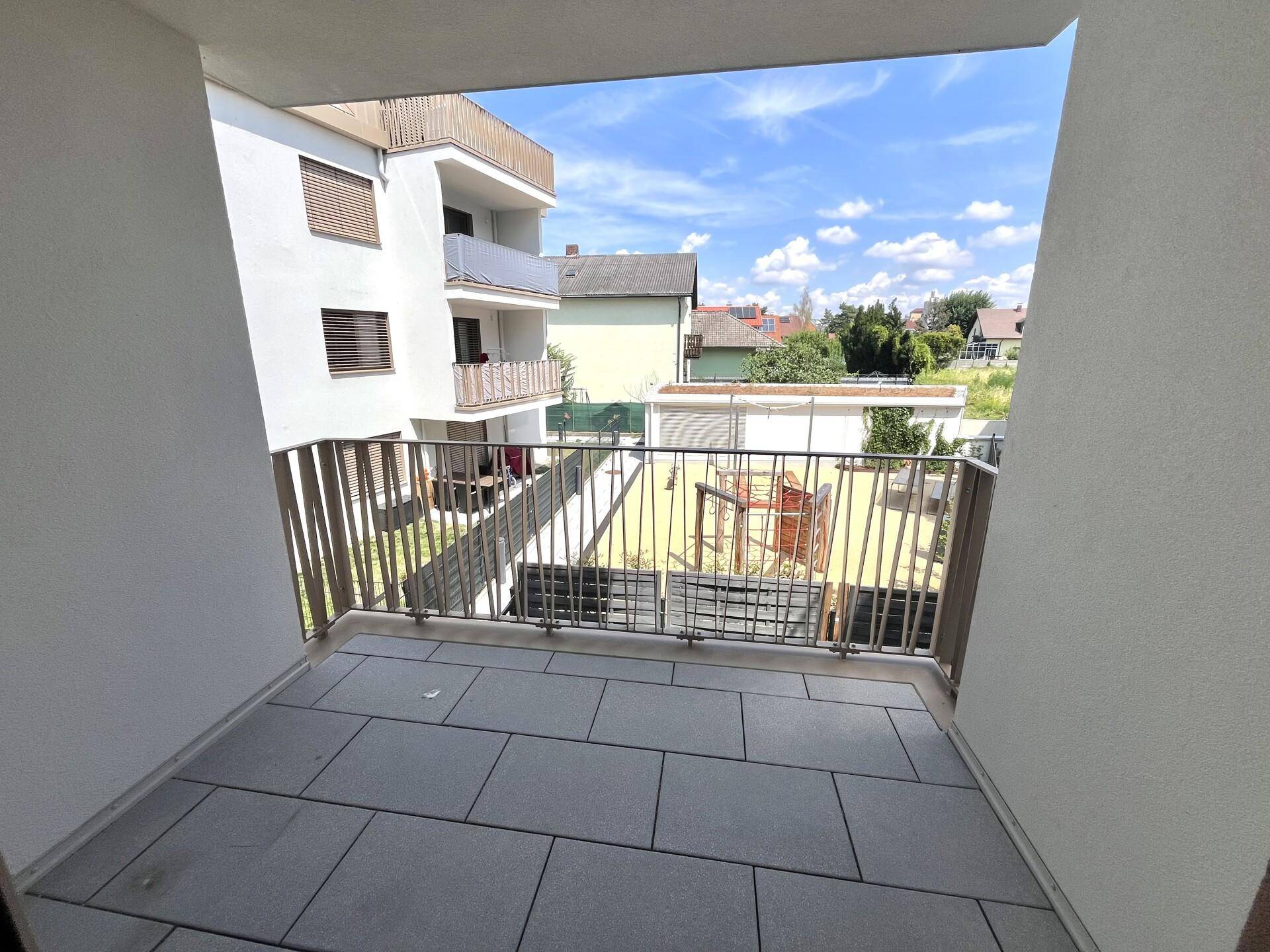 Gefliester Balkon mit Metallgeländer und Blick auf den Innenhof mit Spielplatz und weiteren Gebäuden.