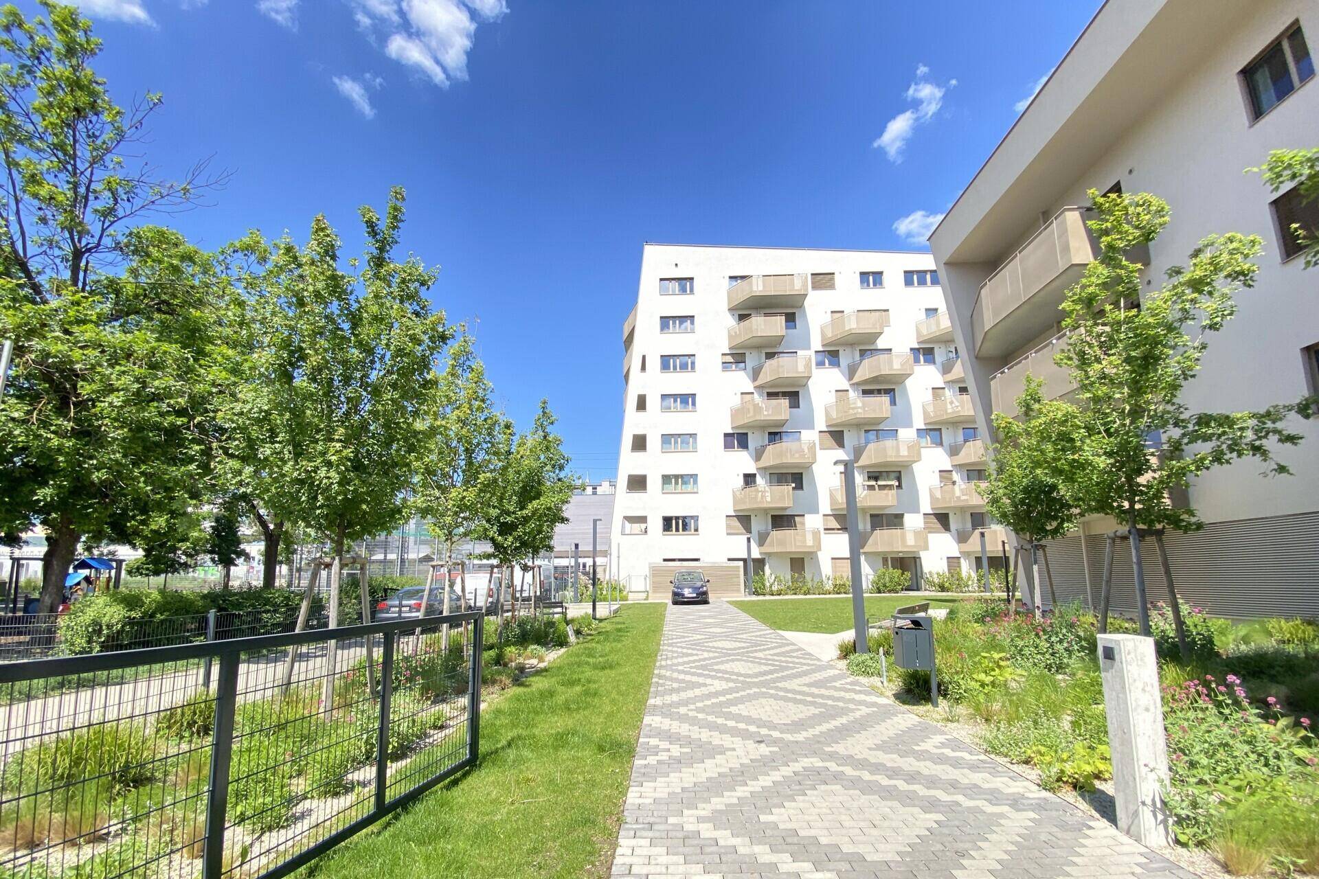 Moderne Wohngebäude mit Balkonen, gepflastertem Weg und grünen Außenanlagen unter blauem Himmel.