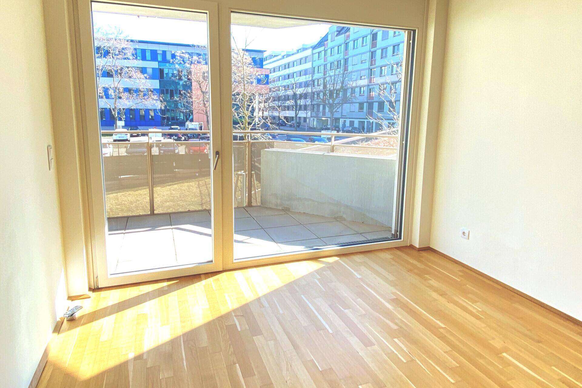 Heller Wohnraum mit Parkettboden und Zugang zu einem sonnigen Balkon.