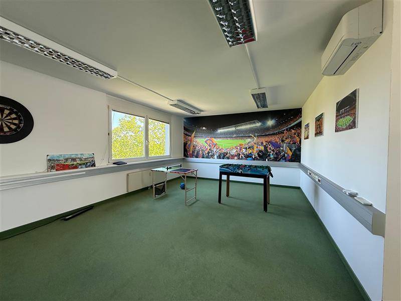 Freizeitraum mit Dartscheibe, Tischfußball und einer großen Wandtapete mit Stadionmotiv.