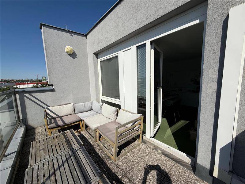 Gemütliche Dachterrasse mit Outdoor-Sofa, Holztisch und Zugang zum Innenbereich durch eine Glastür.