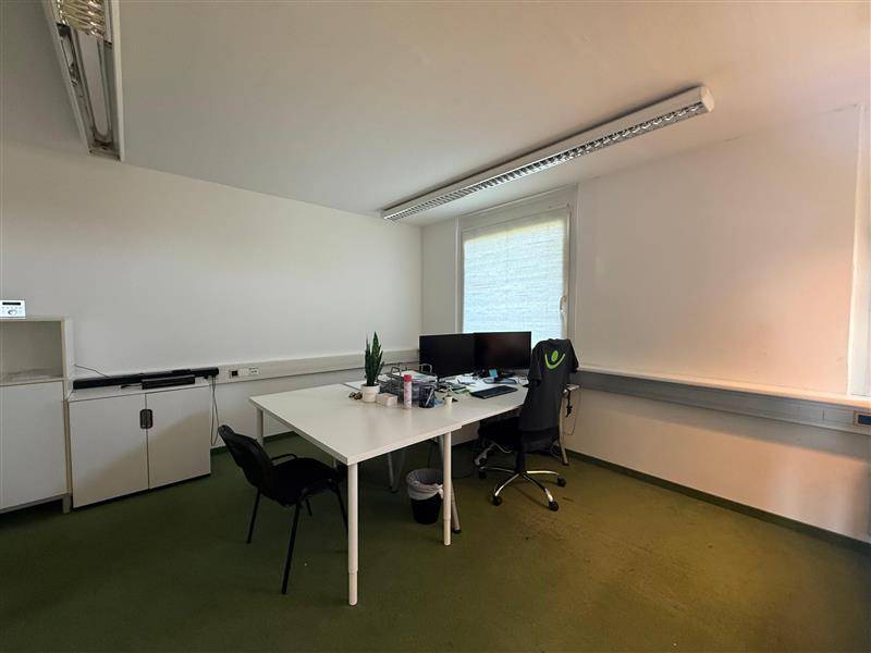 Funktionaler Büroraum mit zwei Arbeitsplätzen, Schreibtischen und einem Fenster mit Jalousien.