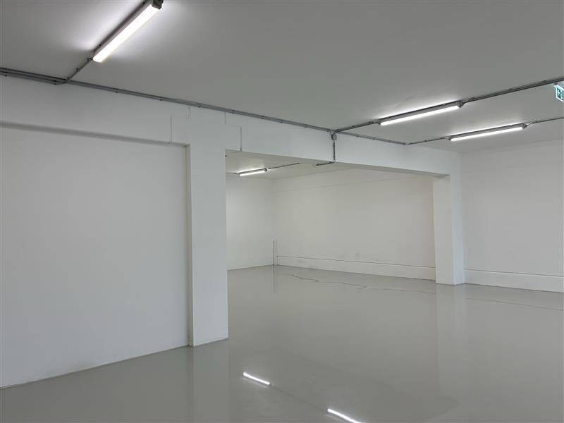 Großer, leerer Bürobereich mit weißen Wänden, glänzendem Boden und sichtbaren Deckeninstallationen.