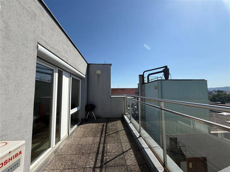 Geräumige Dachterrasse mit Fliesenboden, Glasgeländer und Blick auf die umliegenden Gebäude.