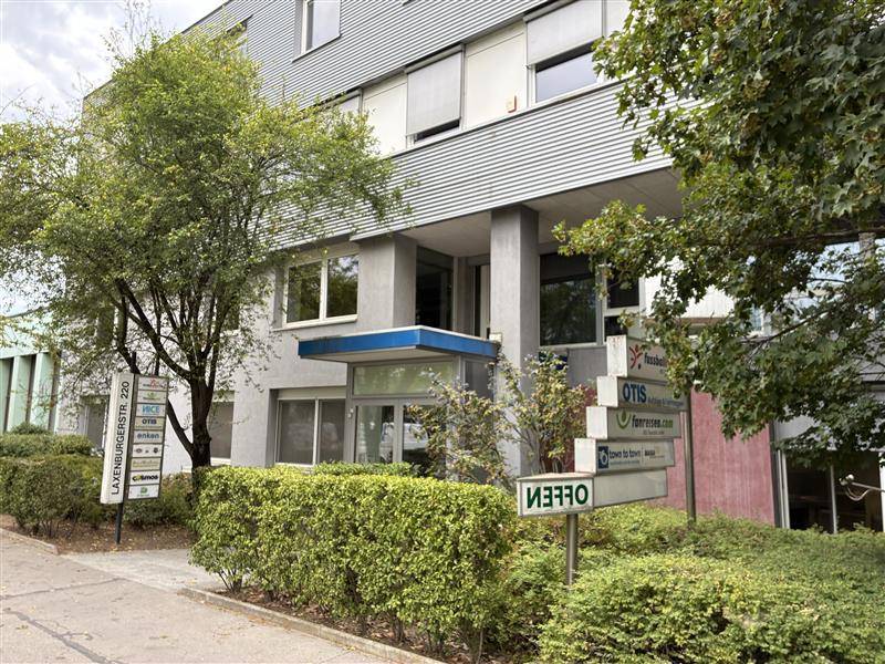 Eingangsbereich eines modernen Geschäftsgebäudes mit Beschilderung und gepflegter Bepflanzung.
