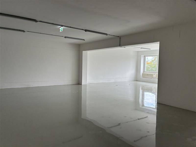 Heller, leerer Raum mit glänzendem Boden und Fenster, das Tageslicht hereinlässt.