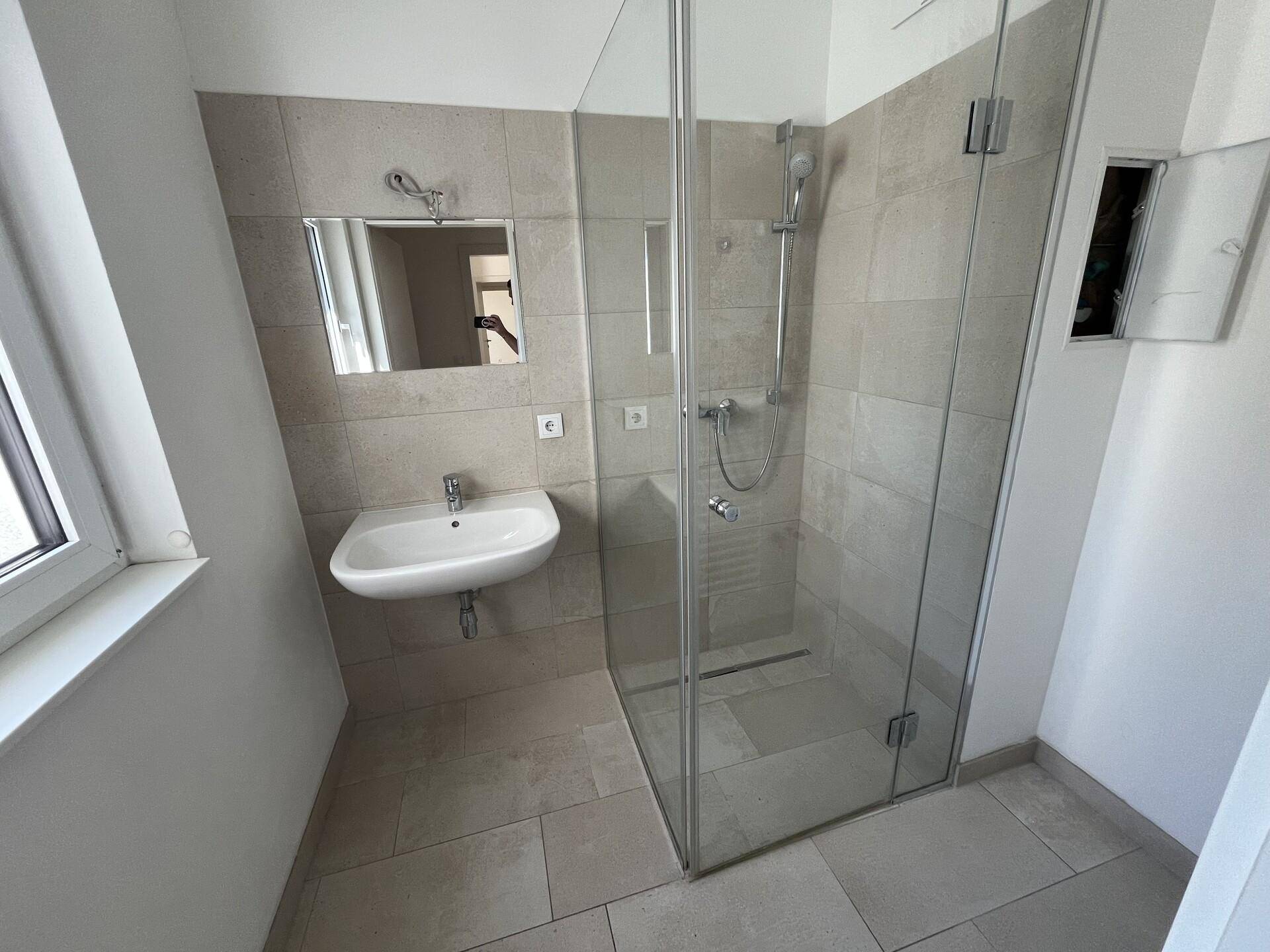 Modernes Badezimmer mit ebenerdiger Dusche, Waschbecken, Spiegel und Fenster.