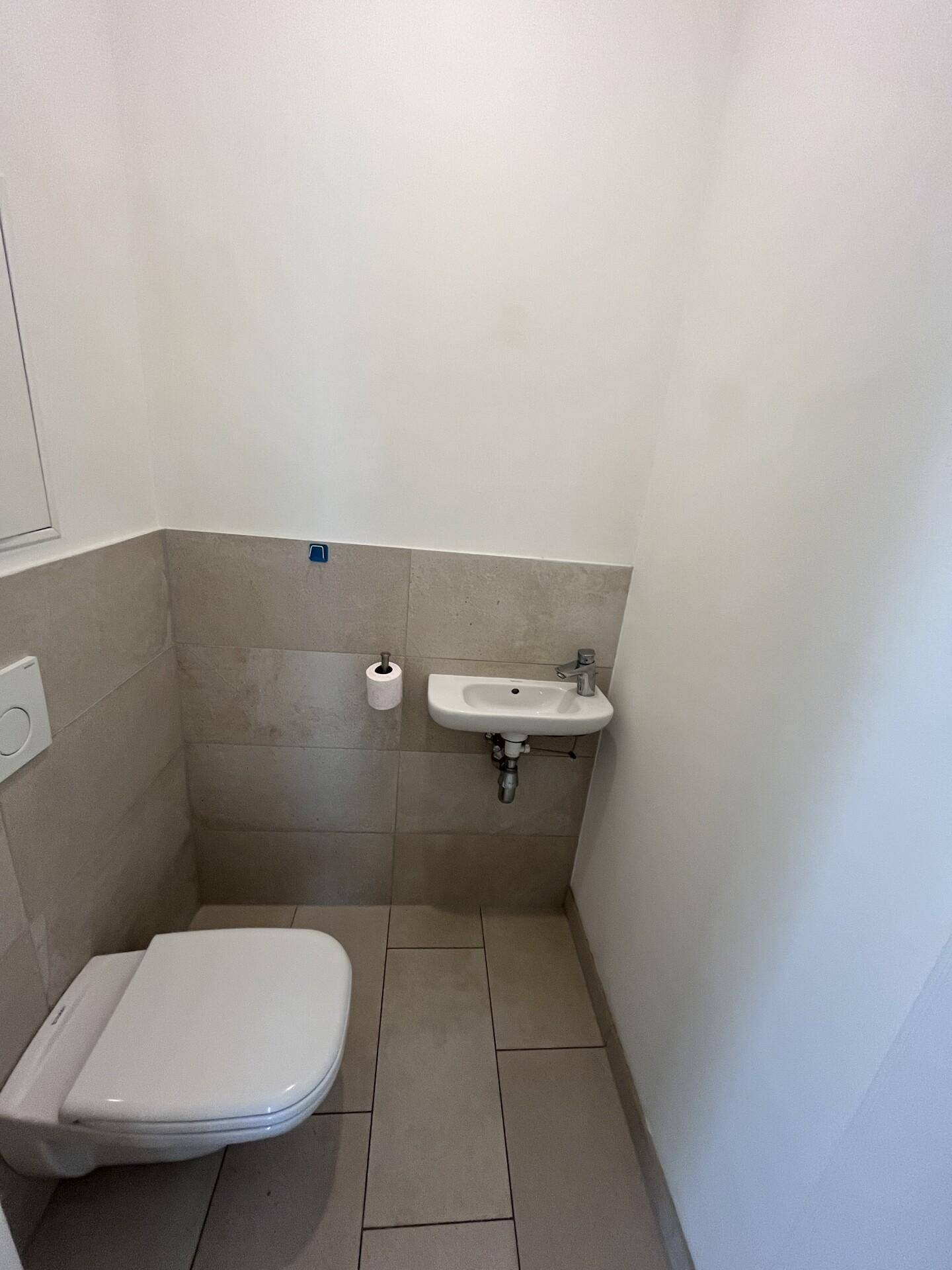 Modernes Gäste-WC mit wandhängendem WC, kleinem Waschbecken und hellen Fliesen.