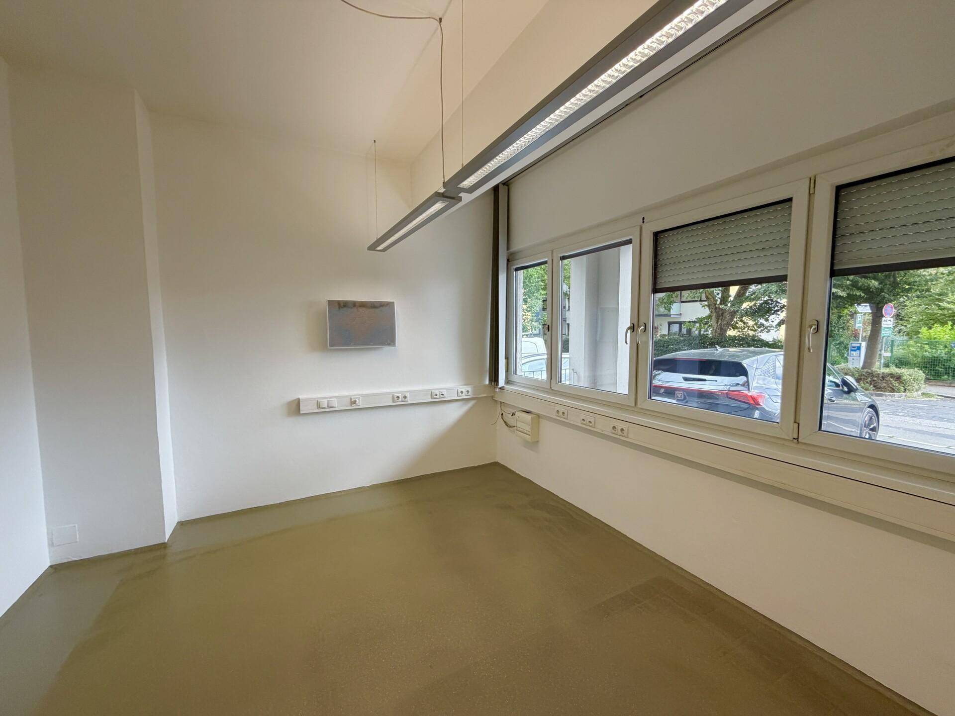 Helles Büro oder Gewerberaum mit großen Fenstern, Rollläden und funktionaler Beleuchtung.