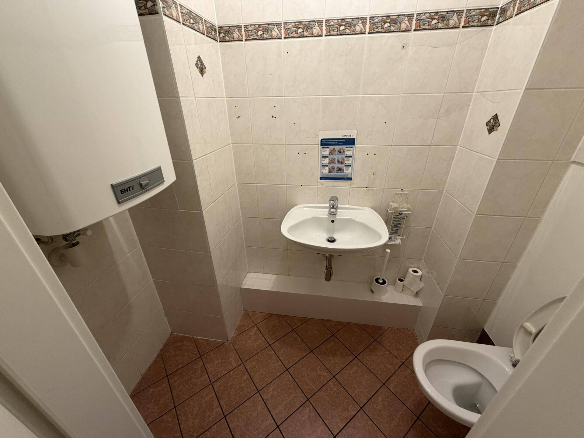 Kleiner Toilettenraum mit Fliesen, Wand-WC, Waschbecken und einem Warmwasserbereiter.