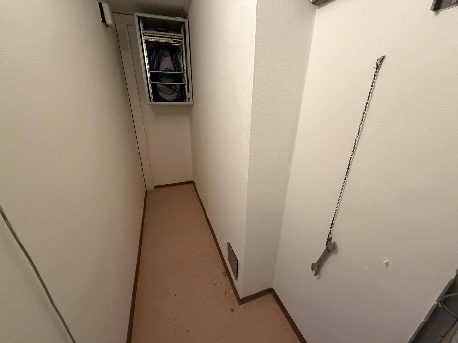 Schmaler Korridor oder Serverraum mit einem an der Wand montierten Serverschrank.