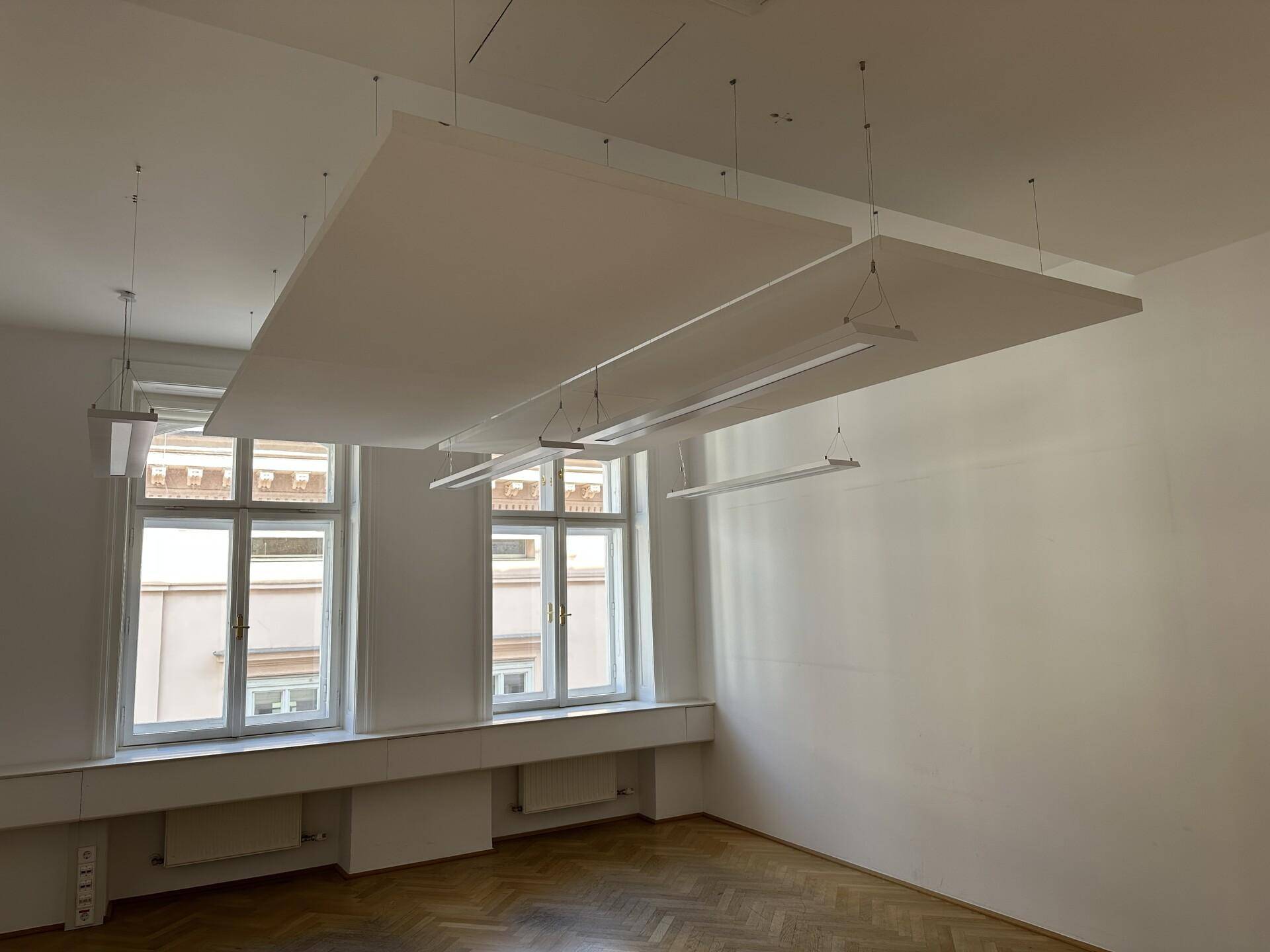 Geräumiges Büro mit Fischgrätparkett, hohen Fenstern und modernen Deckenleuchten für optimale Beleuchtung.