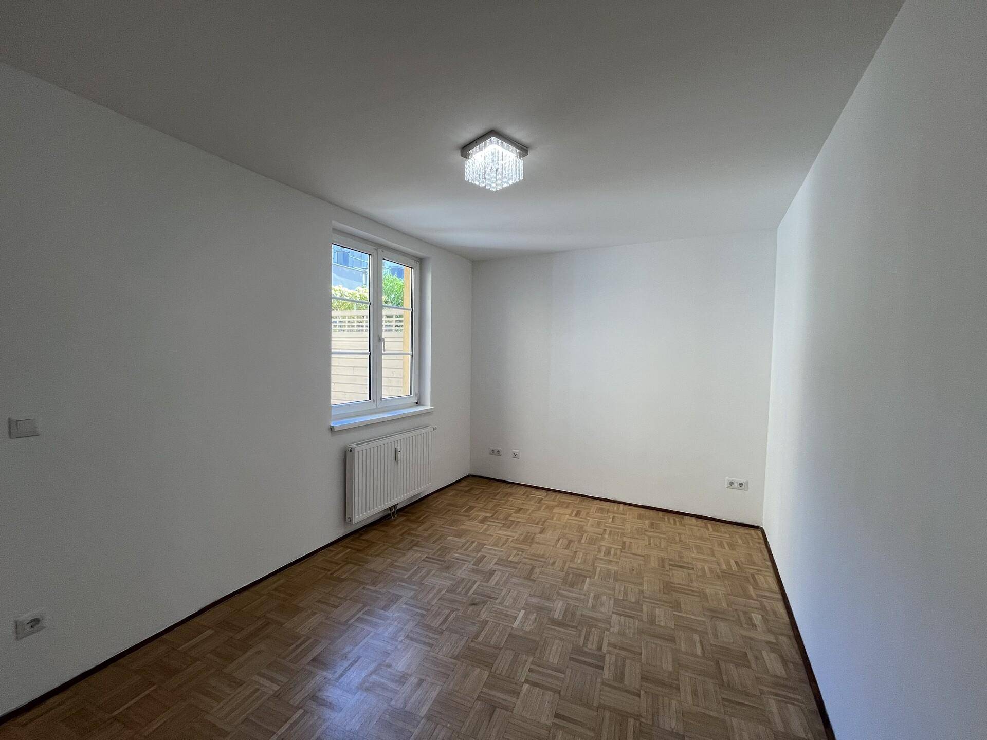 Helles Schlafzimmer mit Parkettboden und einem Fenster, das natürliches Licht hereinlässt.
