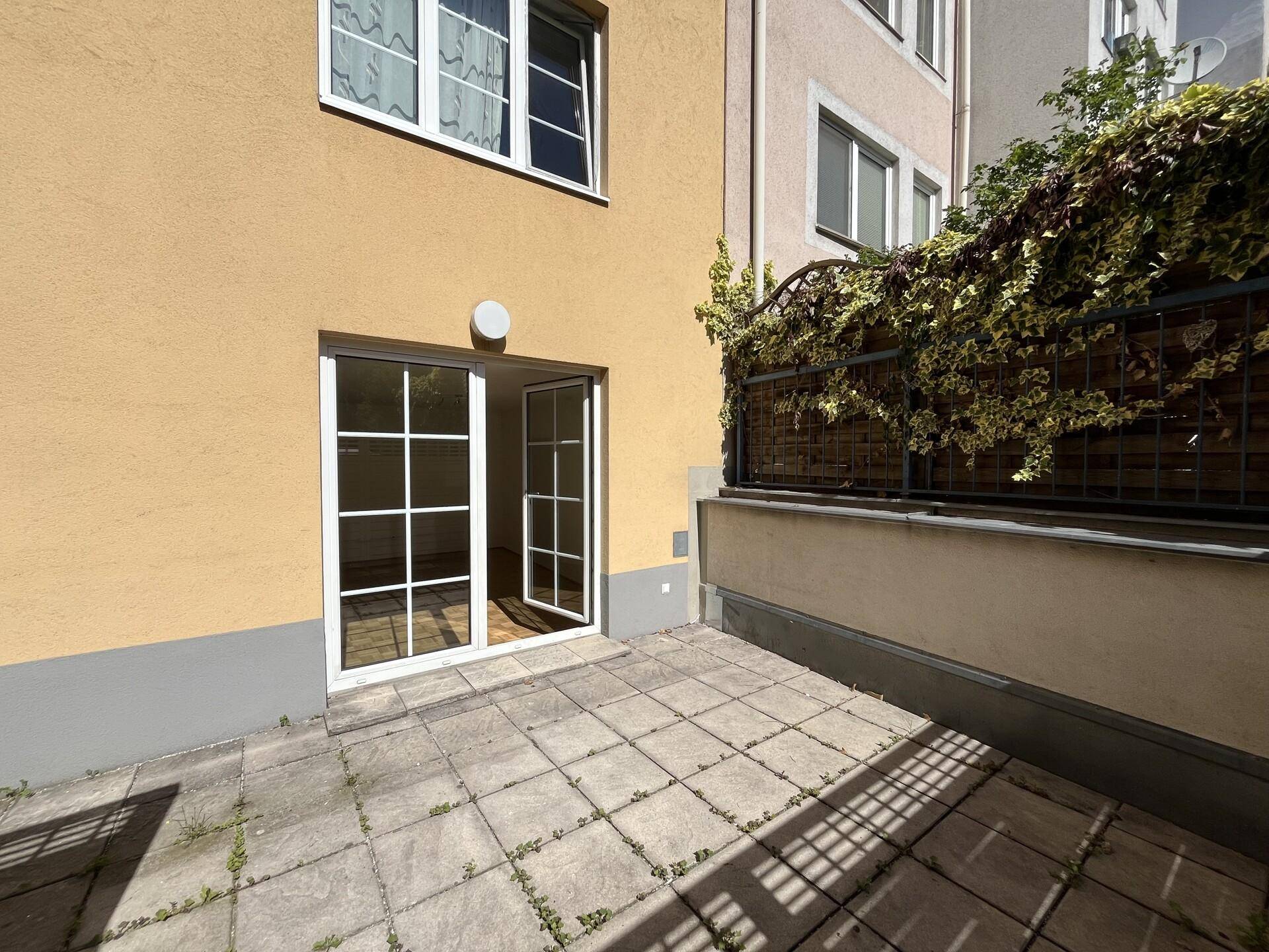 Zugang zu einer gepflasterten Terrasse durch eine große Glastür im Erdgeschoss des Gebäudes.