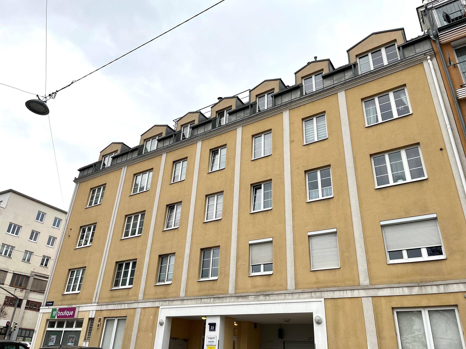 Mehrstöckiges Wohngebäude mit gelber Fassade und zahlreichen Fenstern unter bewölktem Himmel.