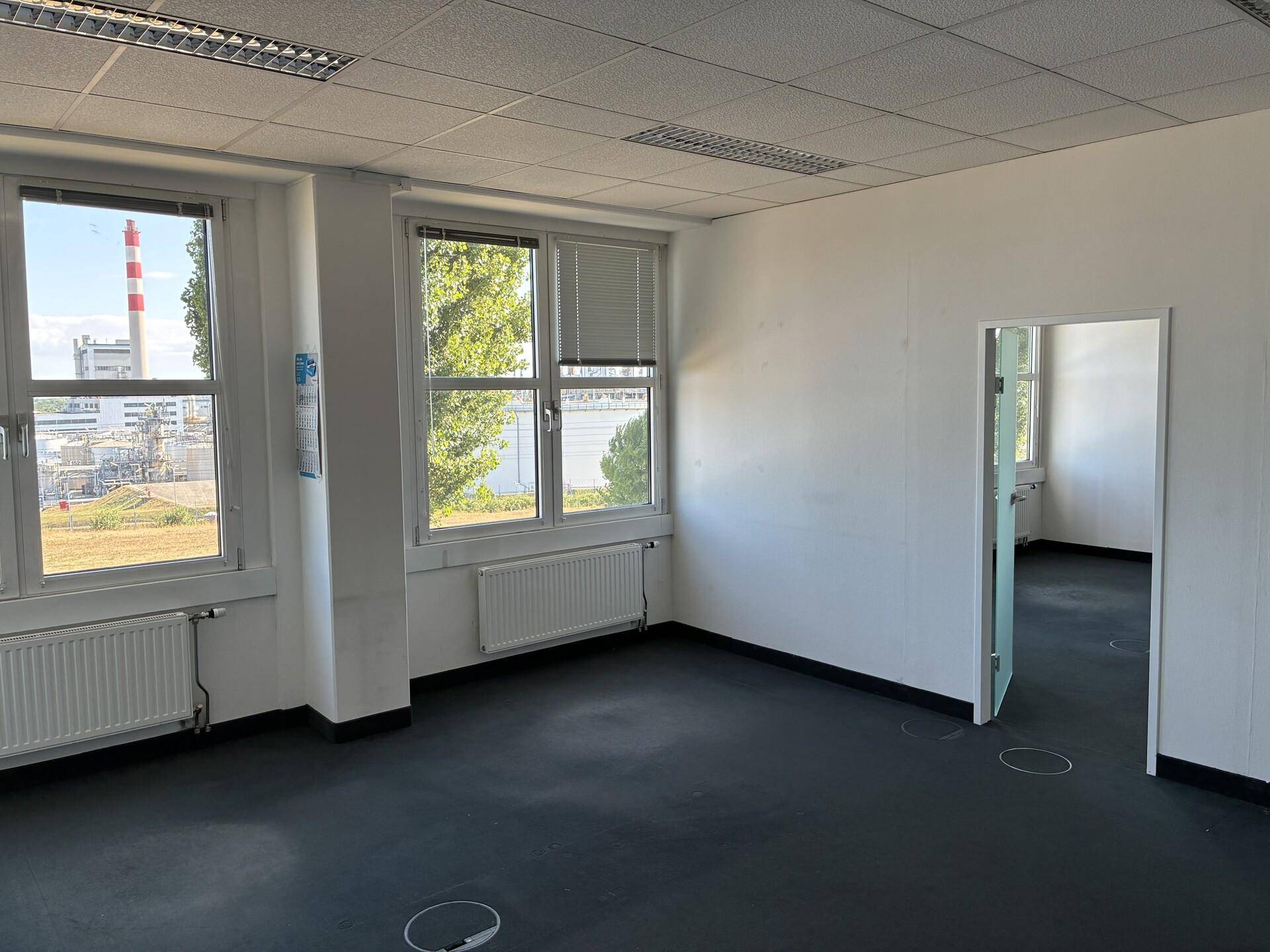 Bürofläche mit Blick auf Industrieanlagen und Wasser, ausgestattet mit Teppichboden und Heizkörpern.
