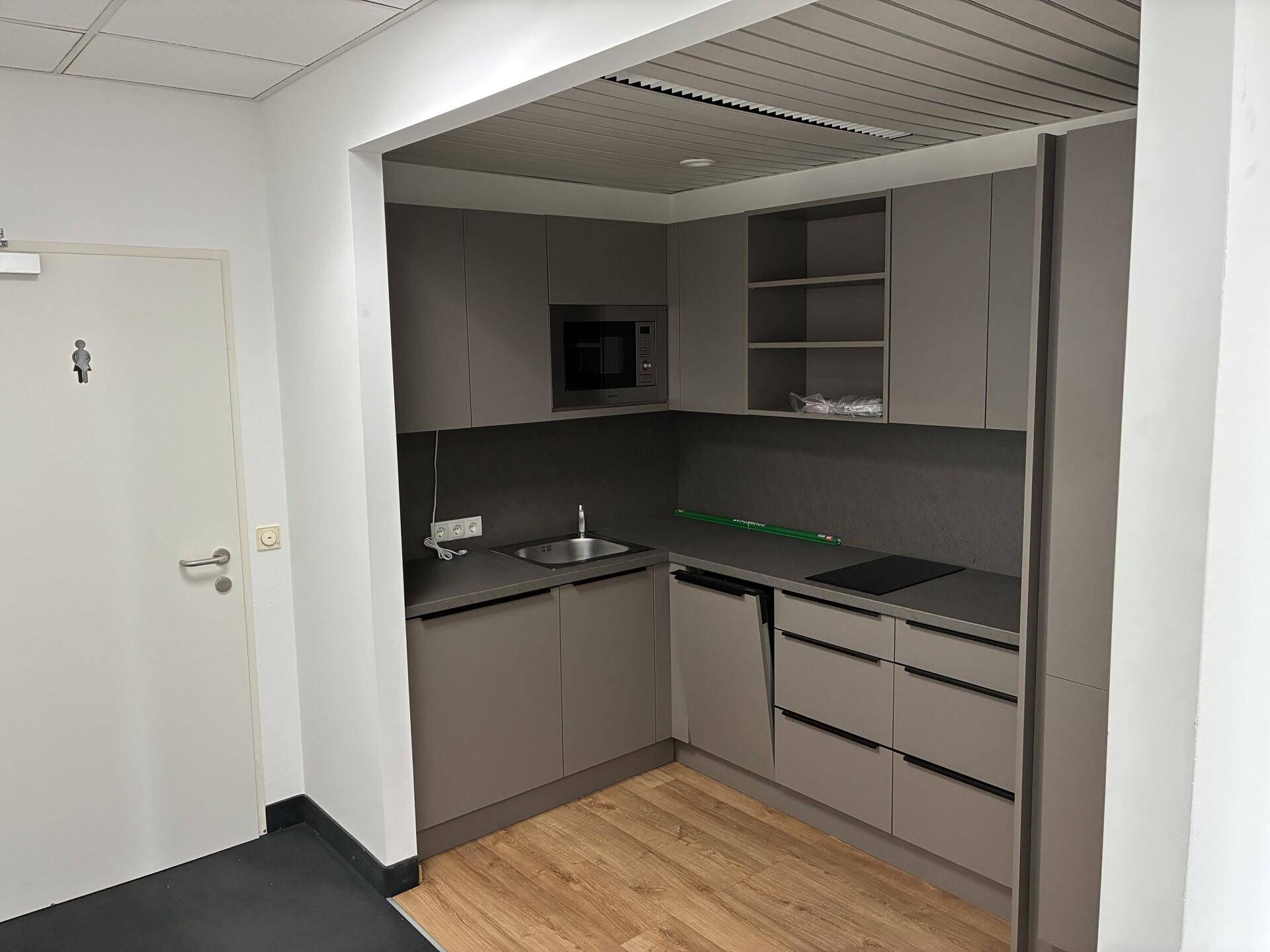 Moderne Küchenzeile in Grau mit integrierter Mikrowelle, Spüle und Kochfeld, ideal für Pausen.