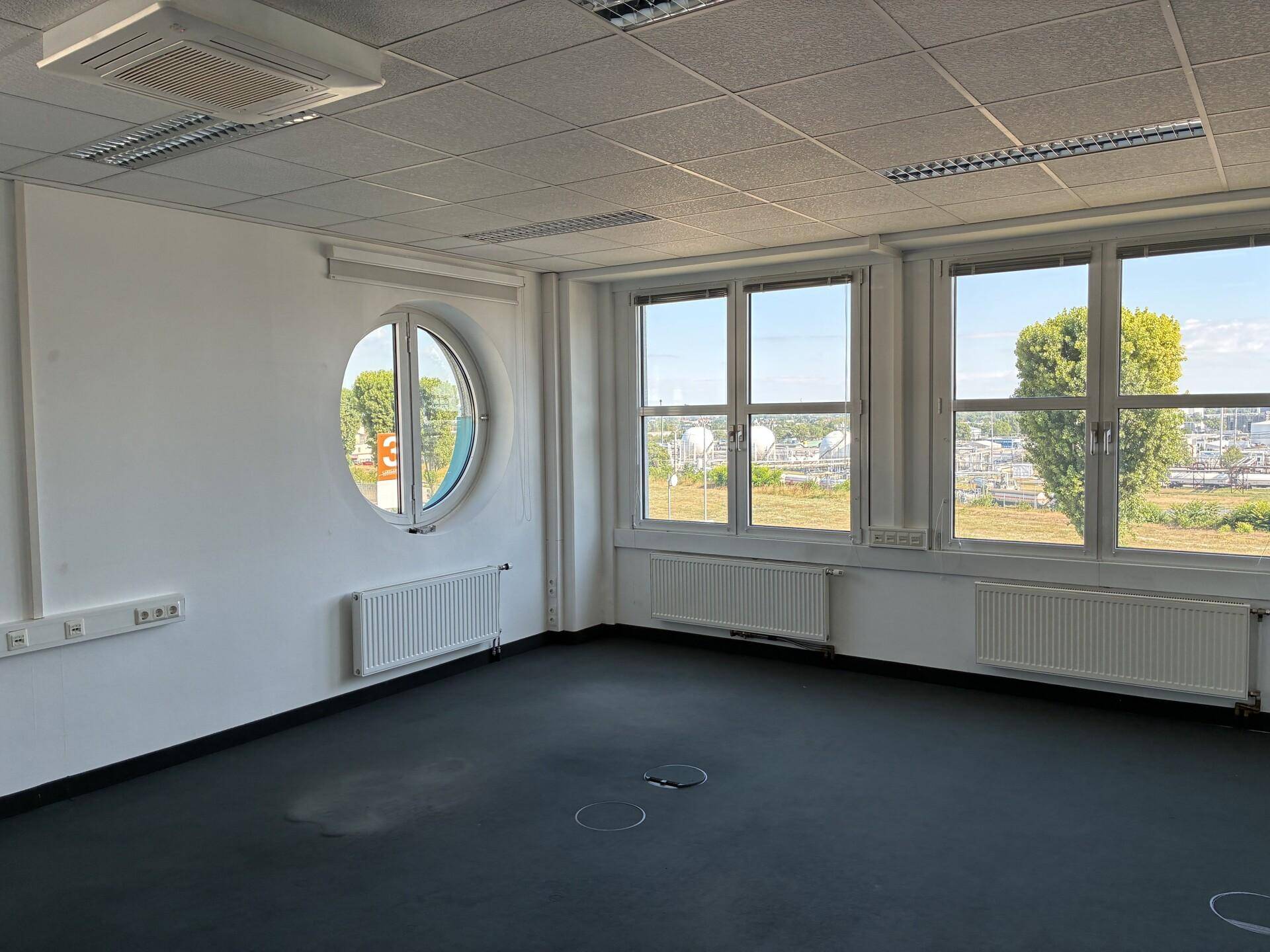 Helles Büro mit einem einzigartigen runden Fenster und weiteren großen Fenstern, die viel Tageslicht bieten.