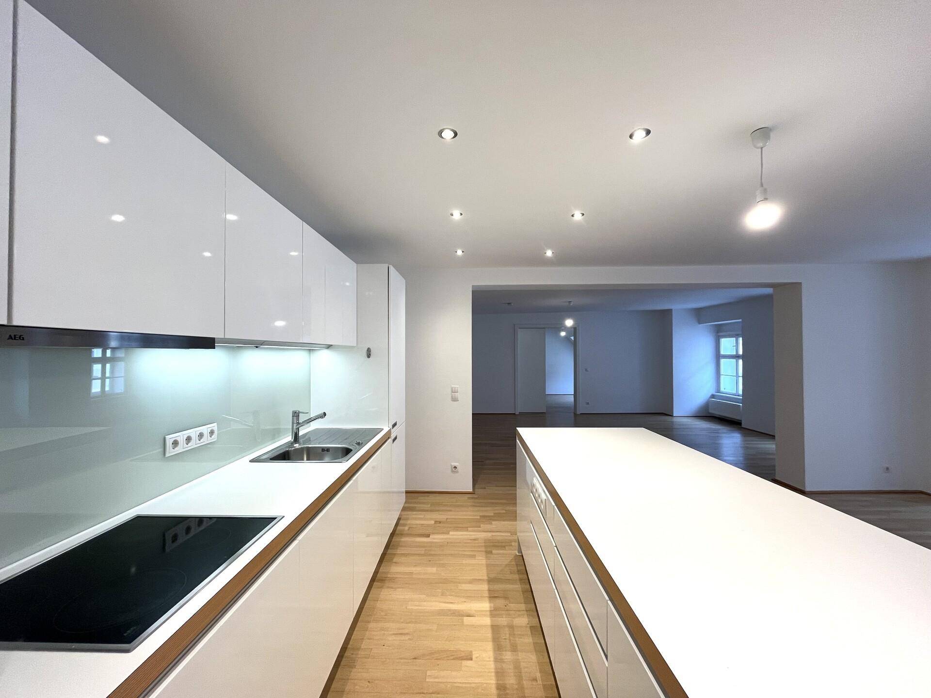 Moderne weiße Küche mit Hochglanzfronten, Induktionskochfeld und langer Kücheninsel, perfekt für Kochliebhaber.