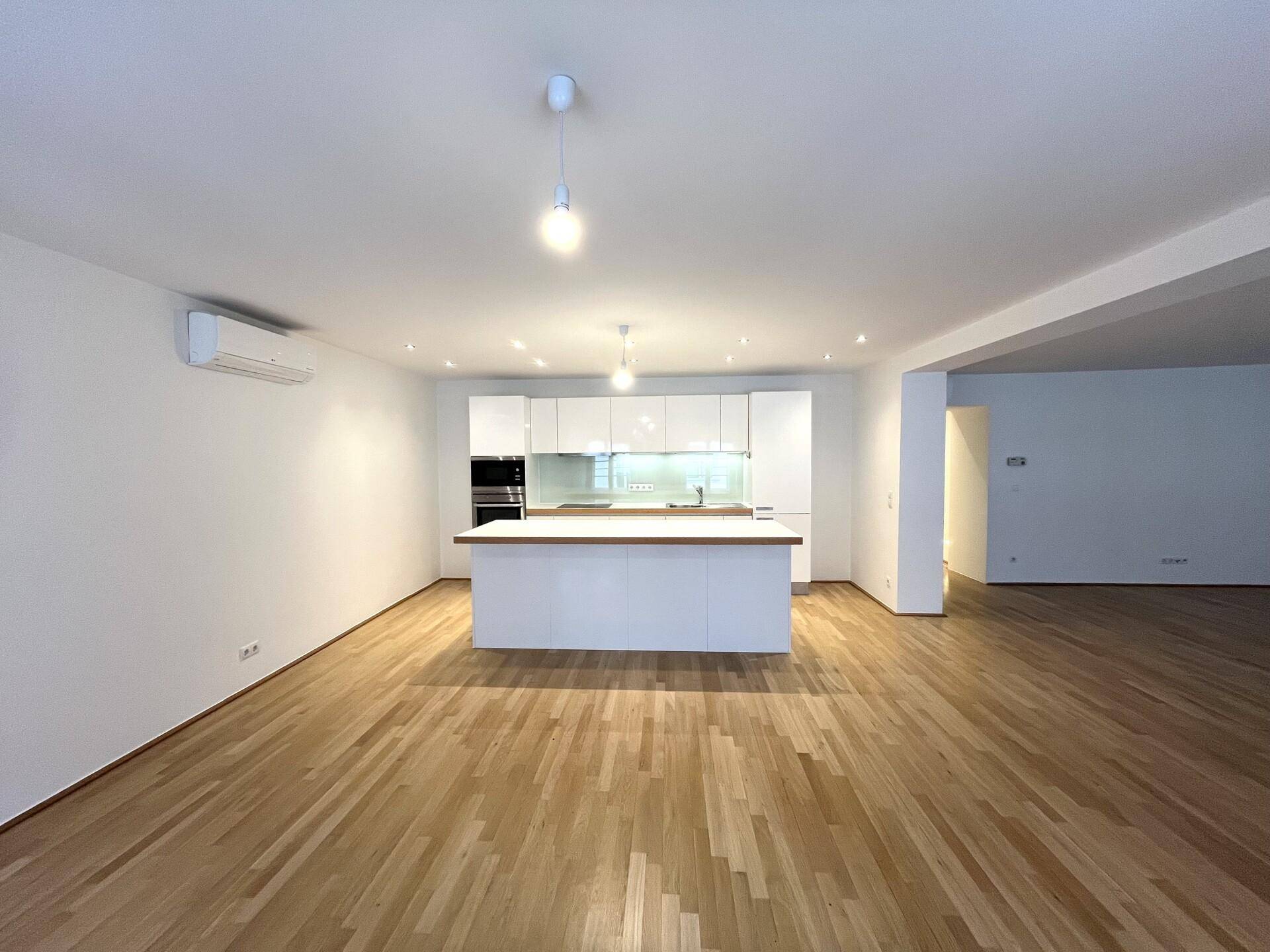 Offener Wohnbereich mit moderner Einbauküche, Kücheninsel und Klimaanlage, ideal für geselliges Beisammensein.