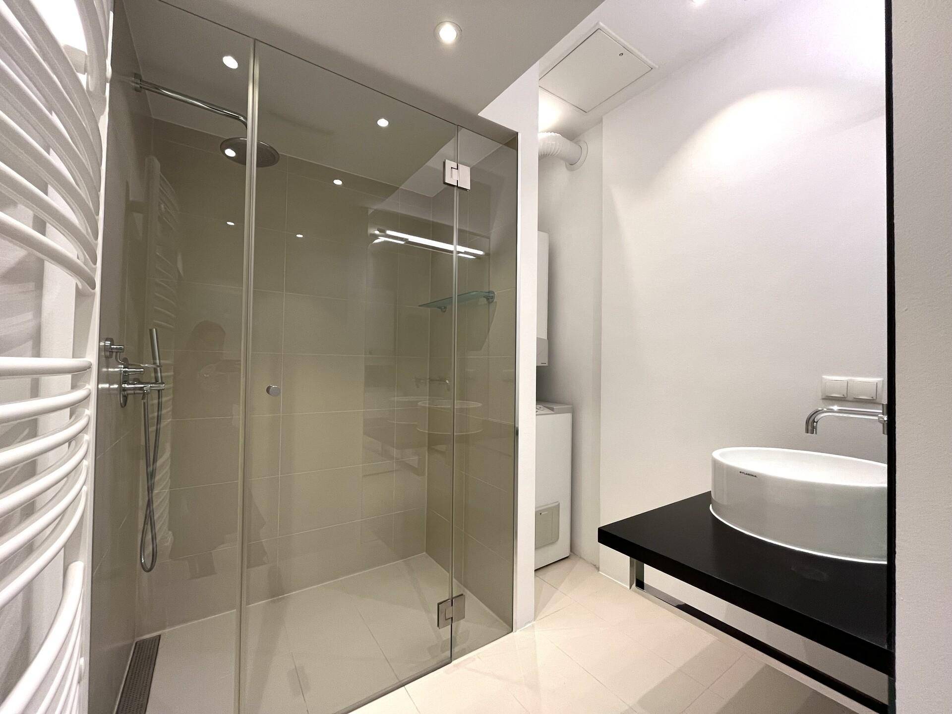 Kompaktes Badezimmer mit Einzelwaschbecken, begehbarer Dusche und beheiztem Handtuchhalter, funktional und modern.