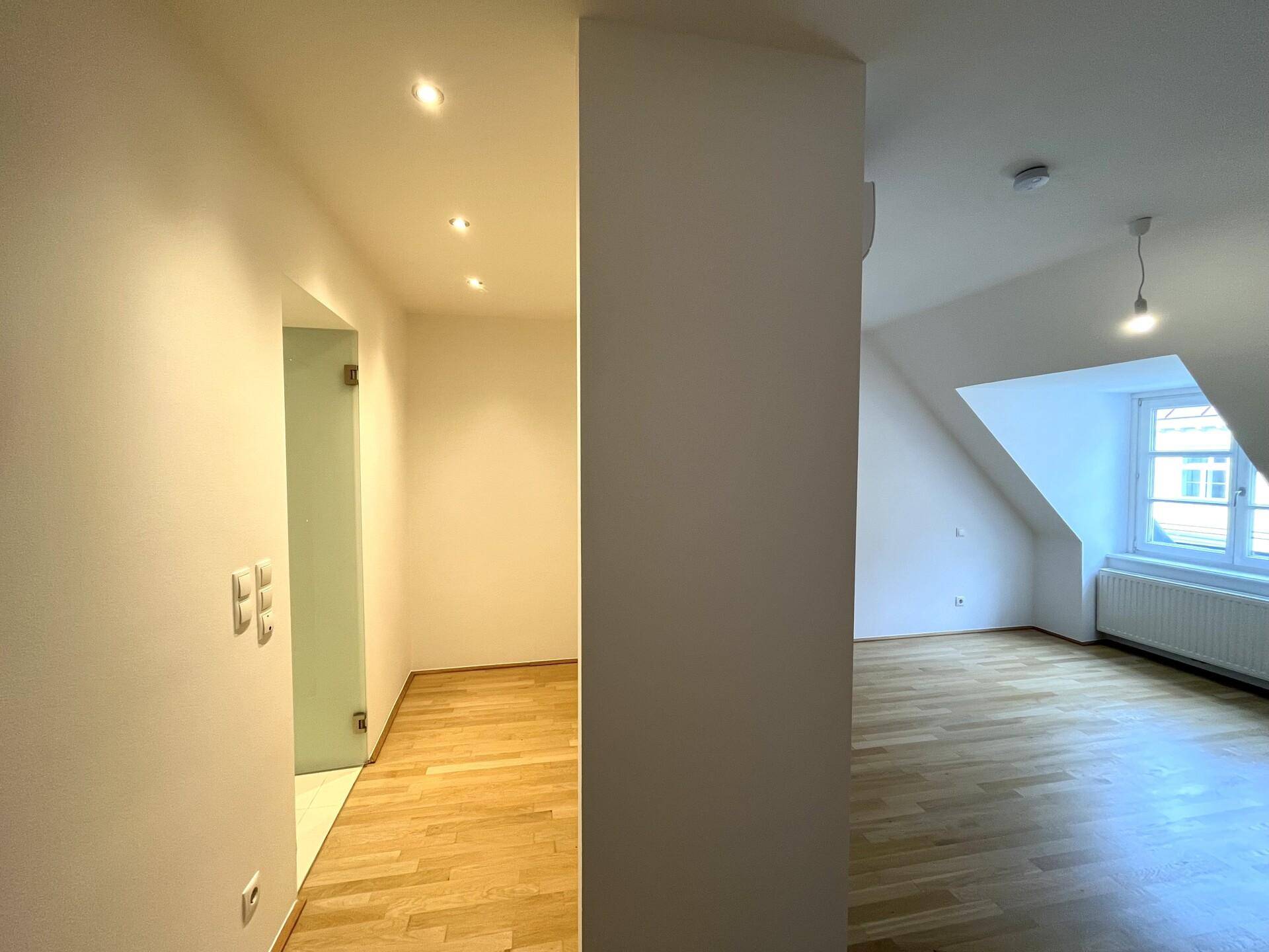 Heller Flur mit Parkettboden, der zu einem Zimmer mit schrägen Wänden und Fenster im Dachgeschoss führt.