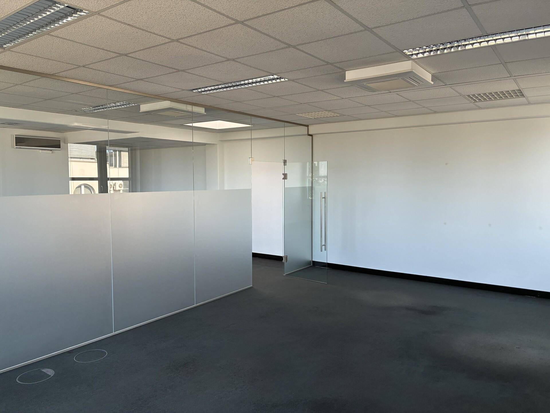 Geräumiges Büro mit modernen Glasabtrennungen, Teppichboden und abgehängter Decke, bereit zur Einrichtung.