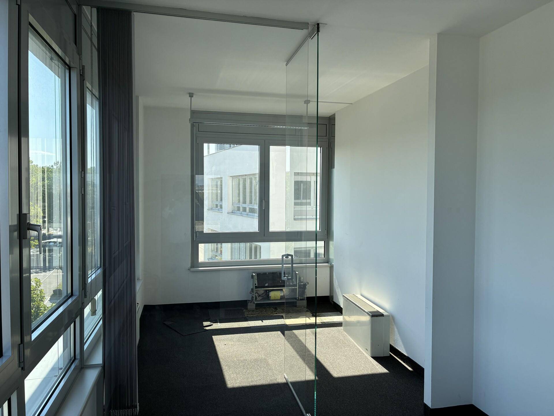 Modernes Büro mit Glaswand, Teppichboden und Blick auf die umliegenden Gebäude.