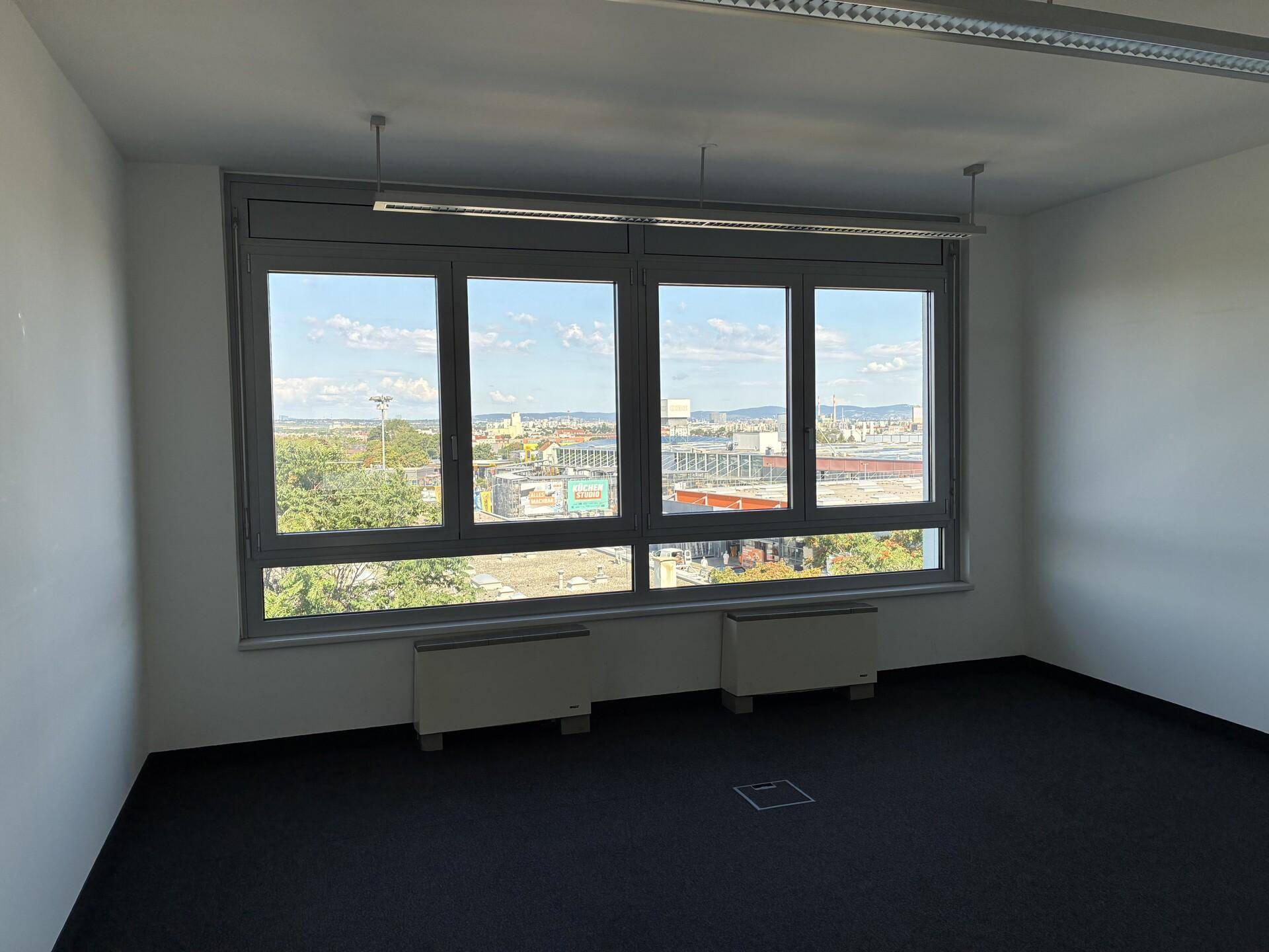 Helles Büro mit weitem Ausblick, Teppichboden und großen Fenstern.