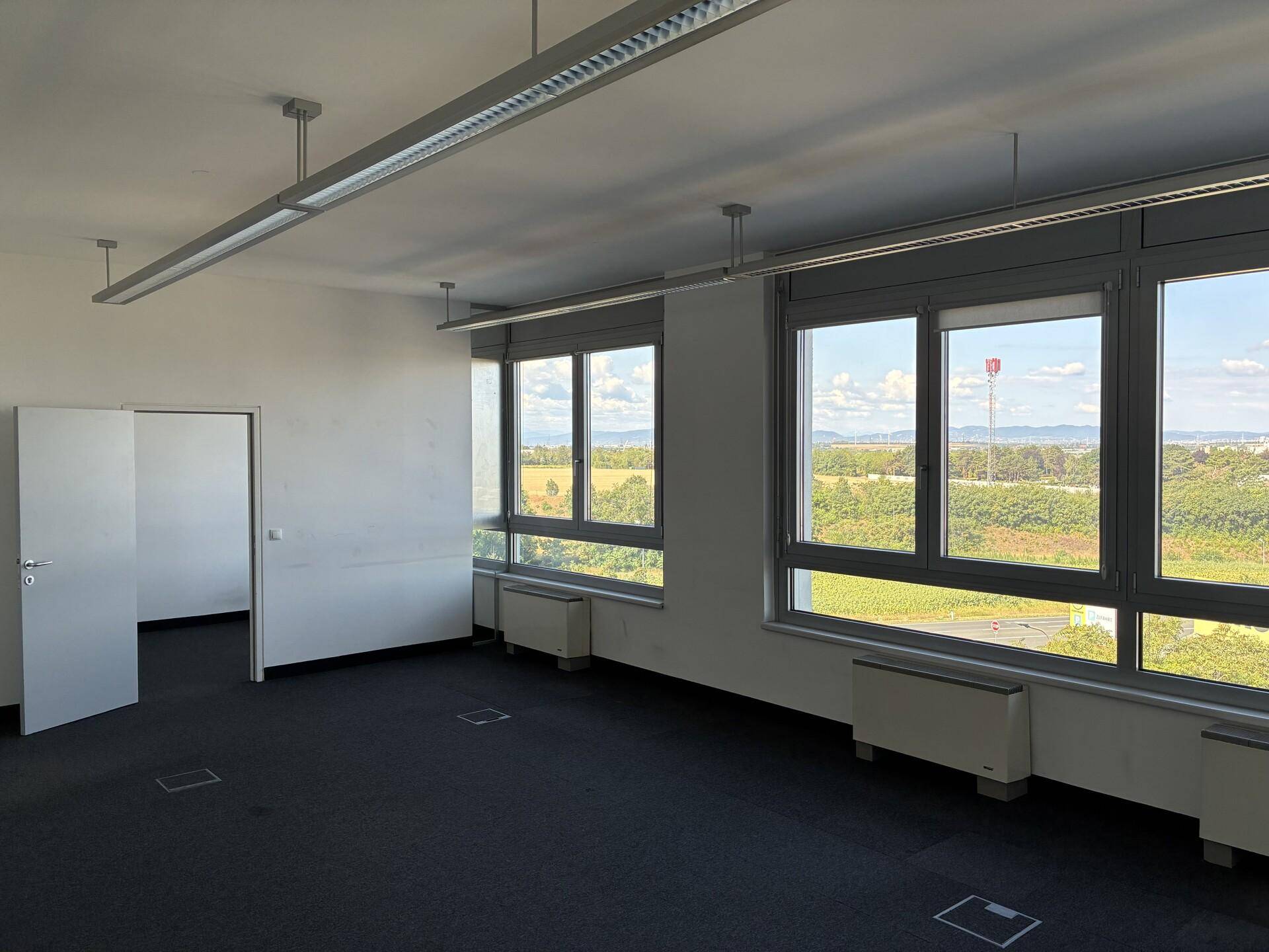 Geräumiges Büro mit Teppichboden, großen Fenstern und weitem Blick ins Grüne.
