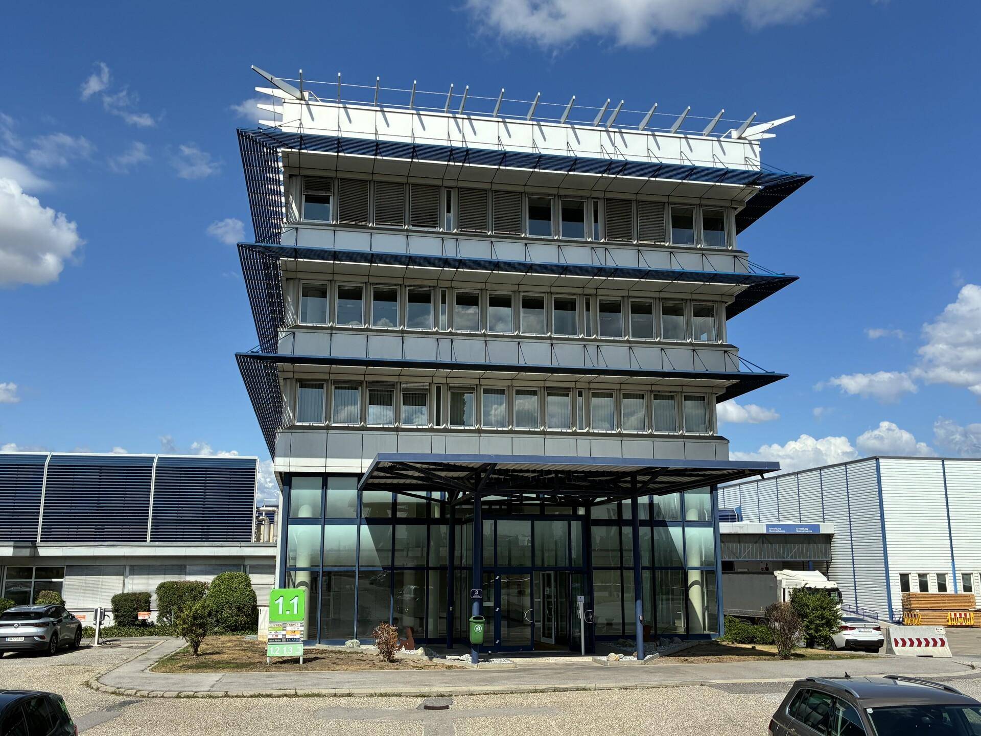 Modernes Bürogebäude mit Glasfassade und mehreren Etagen unter blauem Himmel.