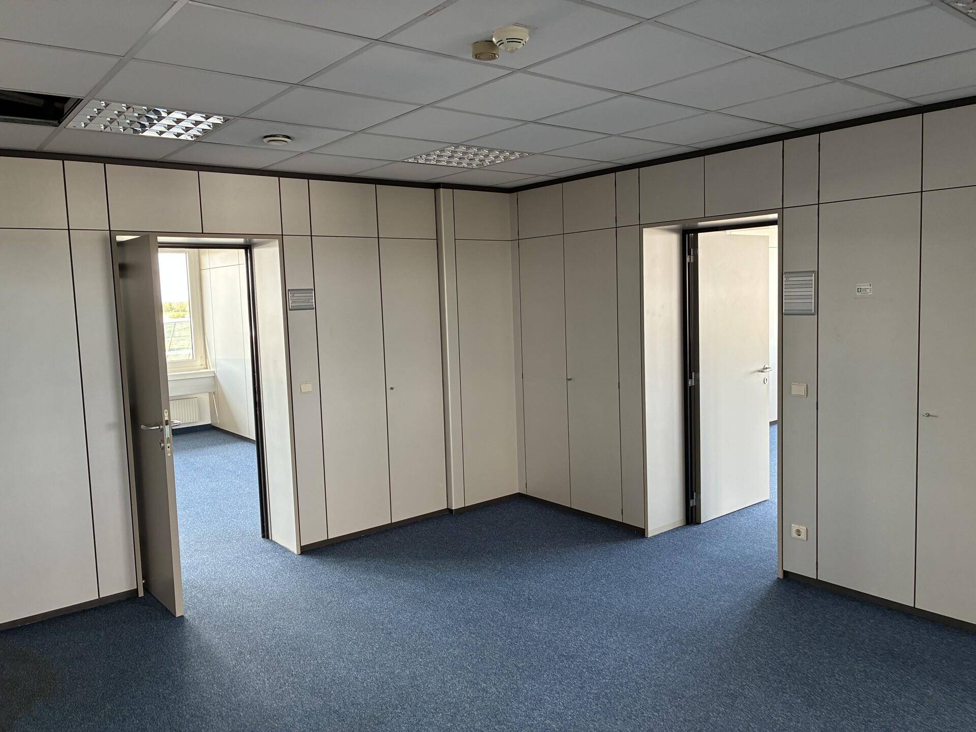 Innenansicht eines Büros mit modularen Trennwänden, blauem Teppich und mehreren Türen.