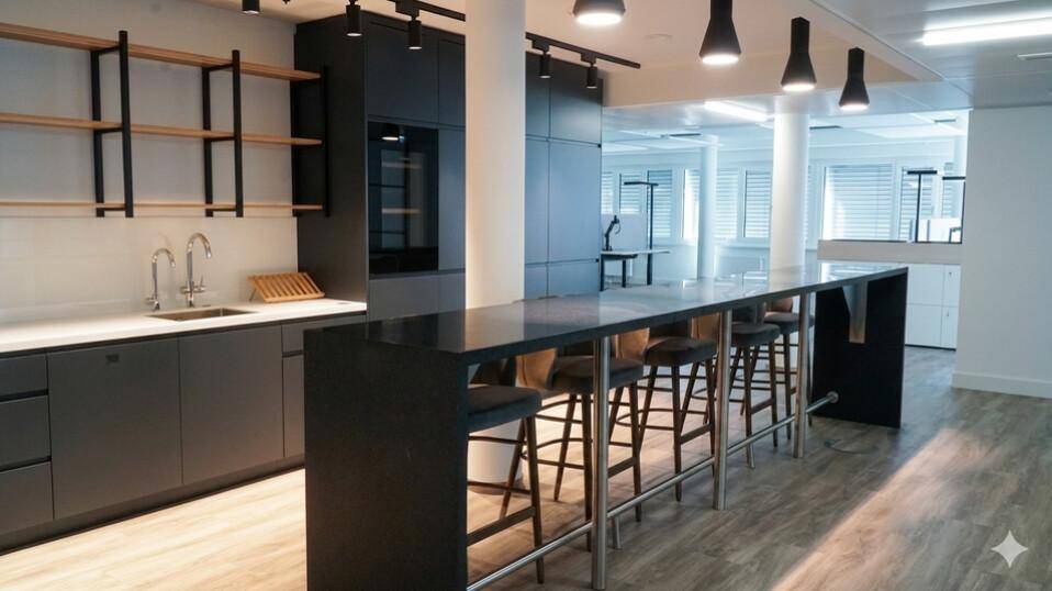 Moderne Teeküche mit dunklen Schränken, langer Bar und Hockern, ideal für Pausen und informelle Treffen.
