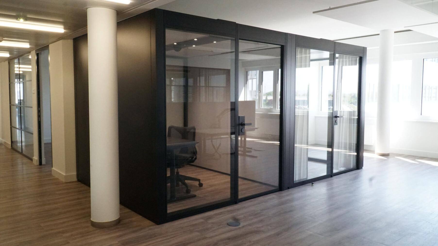 Großraumbüro mit modularen Glasbüros und Holzboden, bietet flexible Arbeitsbereiche und viel Licht.